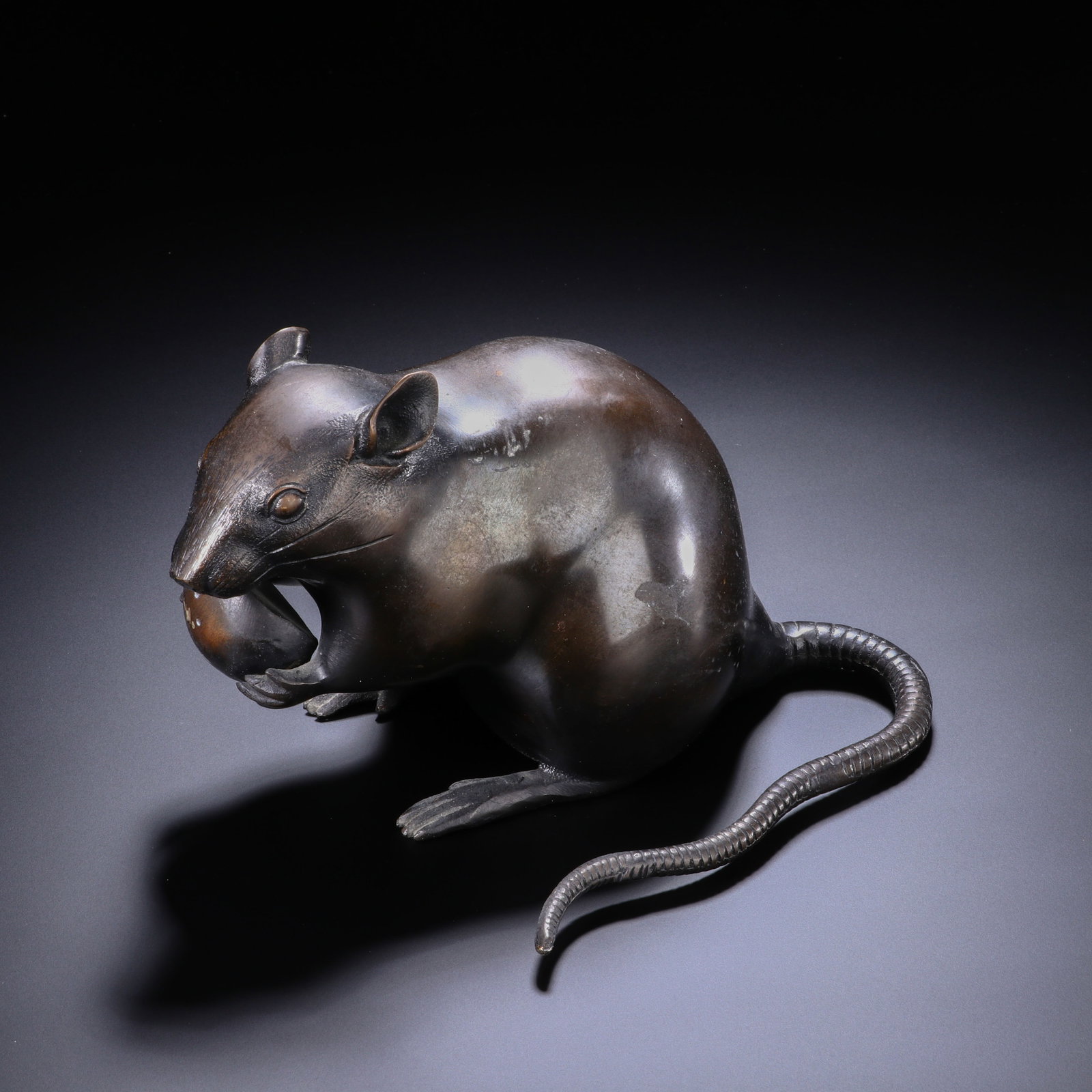 CHINESE BRONZE RAT FIGURE: Dimensions:H. 10.5 cm. W. 16 cm. A fine Chinese bronze figure of a rat, depicted in a naturalistic seated pose holding a fruit in its front paws. The piece features a smooth, dark patina with subtle h