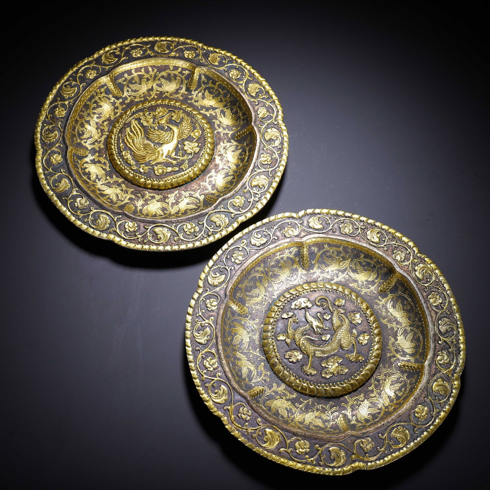 PAIR OF CHINESE GILT-BRONZE DRAGON AND PHOENIX DISHES: Dimensions:L. 20.5 cm. W. 20.5 cm. H. 2 cm. Weight 940 grams. A fine pair of Chinese gilt-bronze lobed dishes, each featuring a dark bronze base with intricate gilt decoration. The central