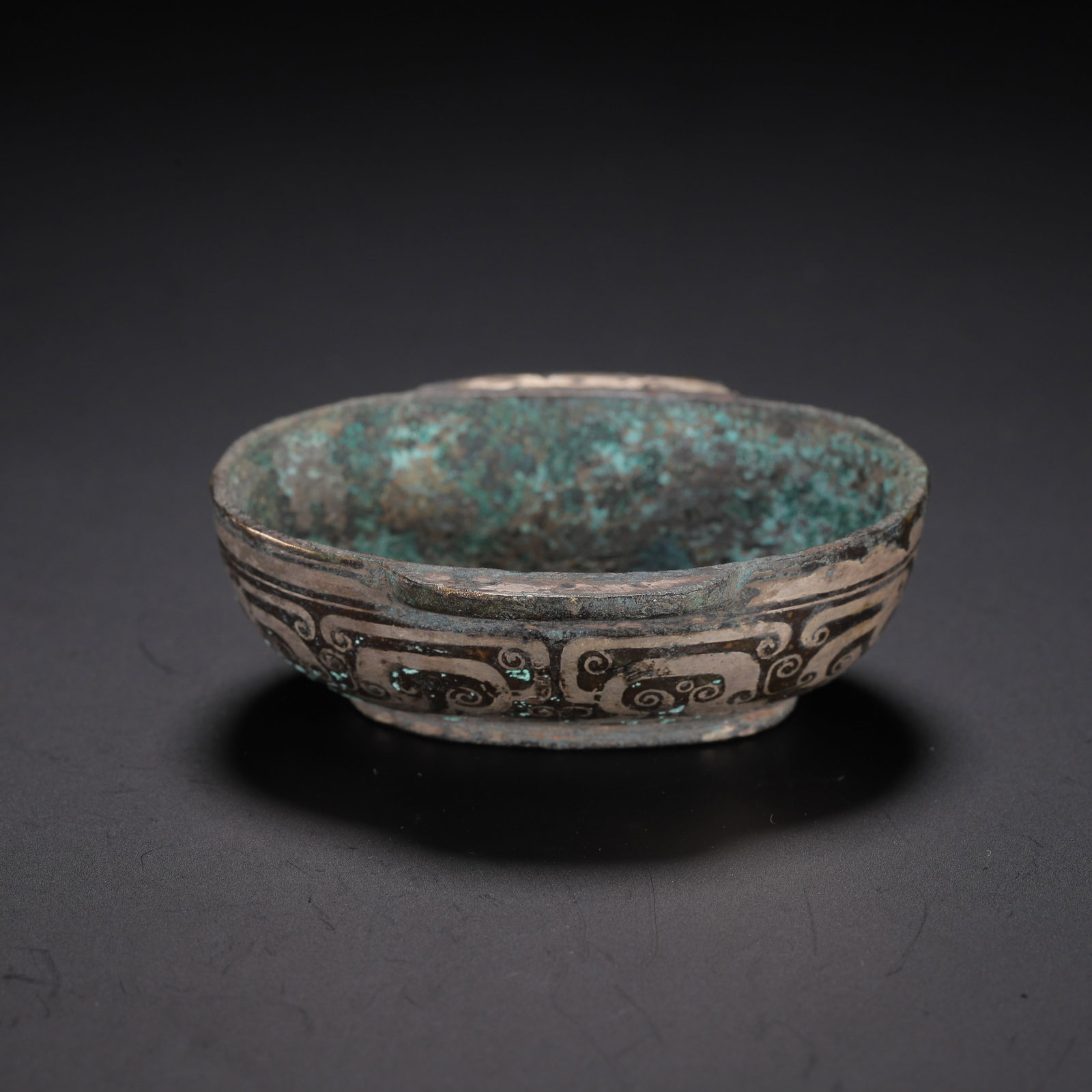 CHINESE SILVER-INLAID BRONZE CUP: Dimensions:L. 6.5 cm. W. 5.5 cm. H. 2.3 cm. Weight 60 grams. A Chinese silver-inlaid bronze cup, of shallow oval form with two small lug handles on the rim. The exterior is adorned with intricate