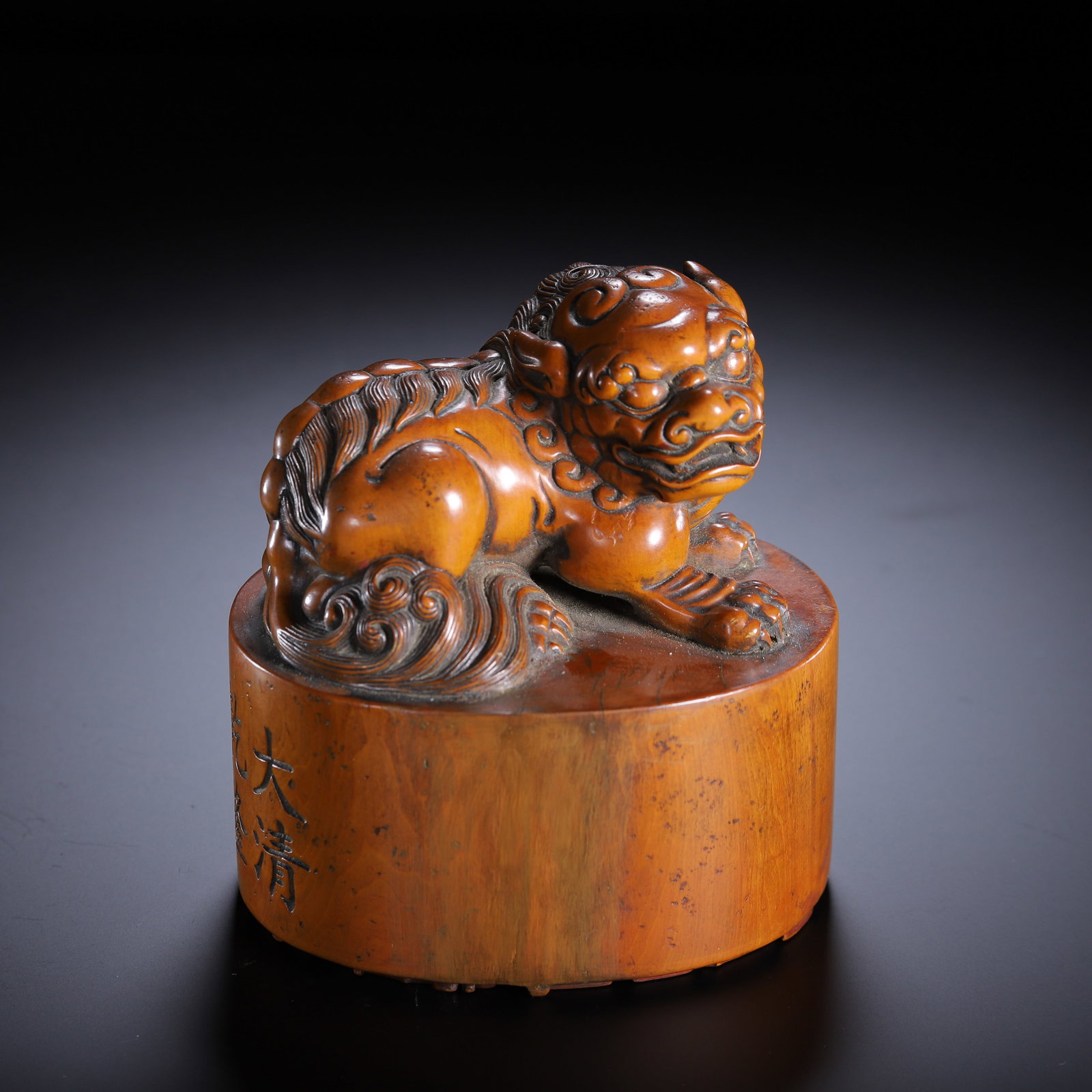 CHINESE HUANGHUALI WOOD LION-FORM SEAL: Dimensions:L. 10 cm. W. 8 cm. H. 11.5 cm. Weight 420 grams. A fine Chinese seal carved from warm amber-hued Huanghuali wood, featuring a recumbent lion (foo dog) finial atop a cylindrical base.