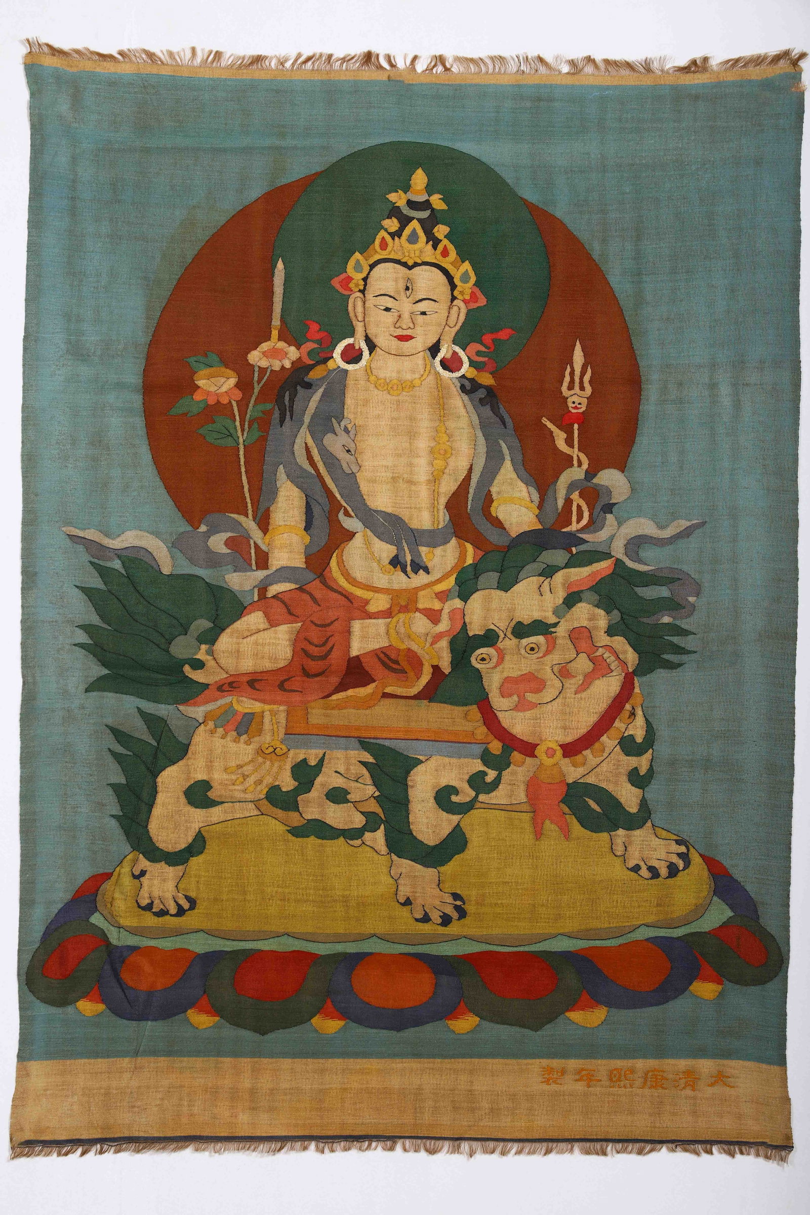 A CHINESE KESI MANJUSHRI THANGKA, KANGXI PERIOD: Dimensions:L. 94 cm. W. 66 cm. A Chinese kesi (silk tapestry) thangka depicting Manjushri, the Bodhisattva of Wisdom, seated majestically atop a snow lion. Woven in vibrant silk threads against a soft
