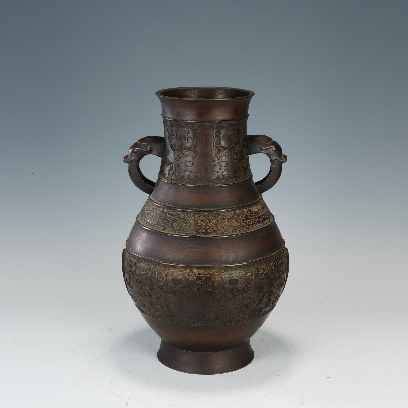A CHINESE BRONZE TAOTIE PATTERN VASE: Dimensions:24x40.5 cm. This Chinese vase is cast from warm patinated bronze, featuring a classic baluster form with a flared rim, two elegantly curved dragon-head handles, and a splayed foot. Its