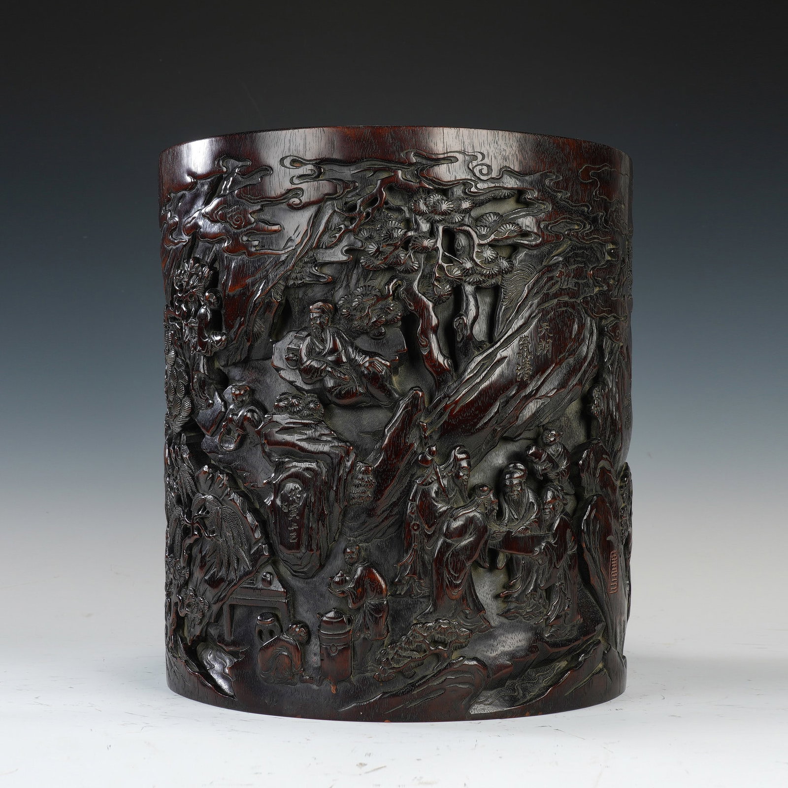CHINESE ZITAN WOOD SCHOLAR BRUSH POT: Dimensions:29.5x32 cm. A fine Chinese Qing dynasty brush pot carved from dense, dark-red zitan (red sandalwood), featuring a high-relief scene of scholars gathering in a pine forest. The