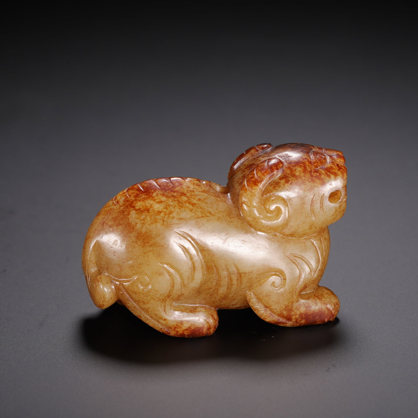 CHINESE HETIAN JADE AUSPICIOUS BEAST CARVING: Dimensions:L. 5.5 cm. H. 4 cm. A fine Chinese Hetian jade carving of an auspicious beast, depicted in a recumbent pose with curled horns and stylized facial features. The warm honey-toned stone displa
