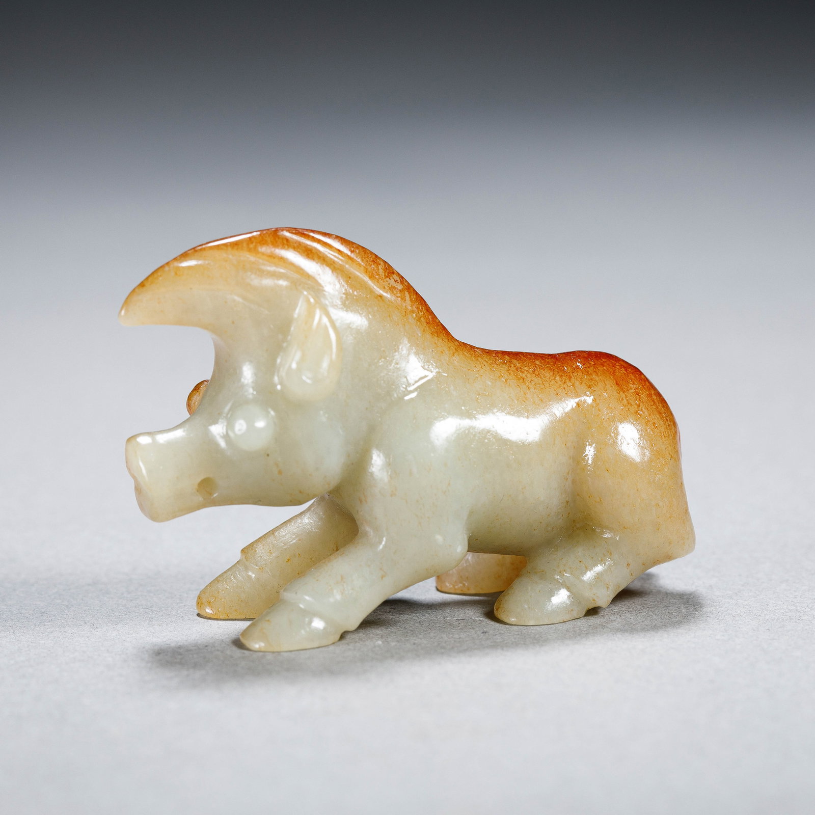 A CHINESE HETIAN JADE ANIMAL PENDANT: Dimensions:L. 5 cm. H. 3.1 cm. Weight 35 grams. A Chinese pendant carved from pale green Hetian jade, featuring a dynamic, striding boar-like mythical creature with natural russet skin