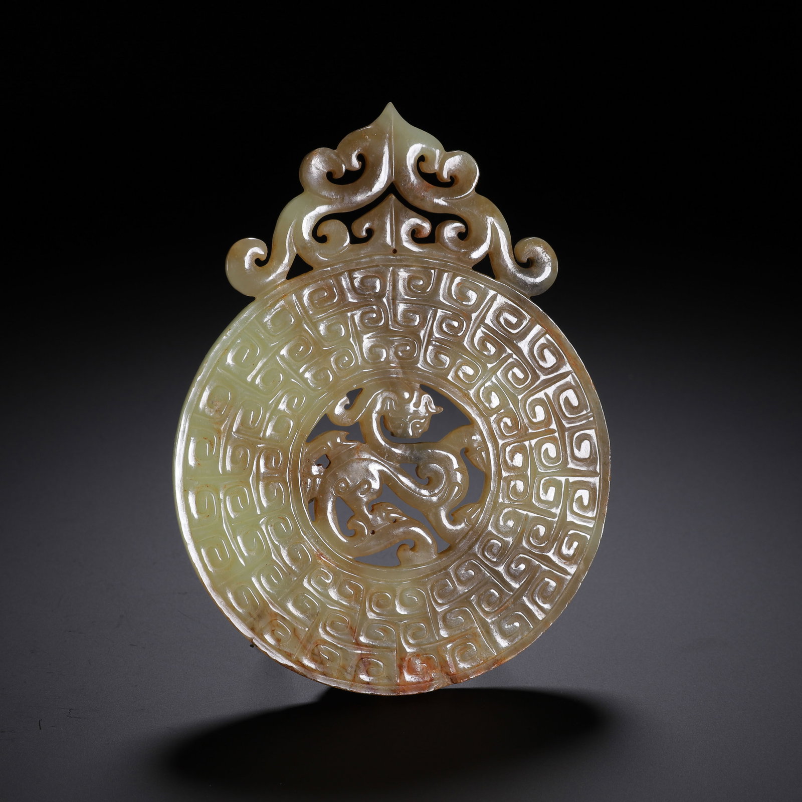 A CHINESE ARCHAIC JADE BI DISC WITH OPENWORK DRAGON: Dimensions:L. 12.5 cm. W. 9.5 cm. Weight 130 grams. A Chinese archaic jade bi disc carved from pale celadon nephrite, featuring a delicate openwork dragon at its center, surrounded by dense,