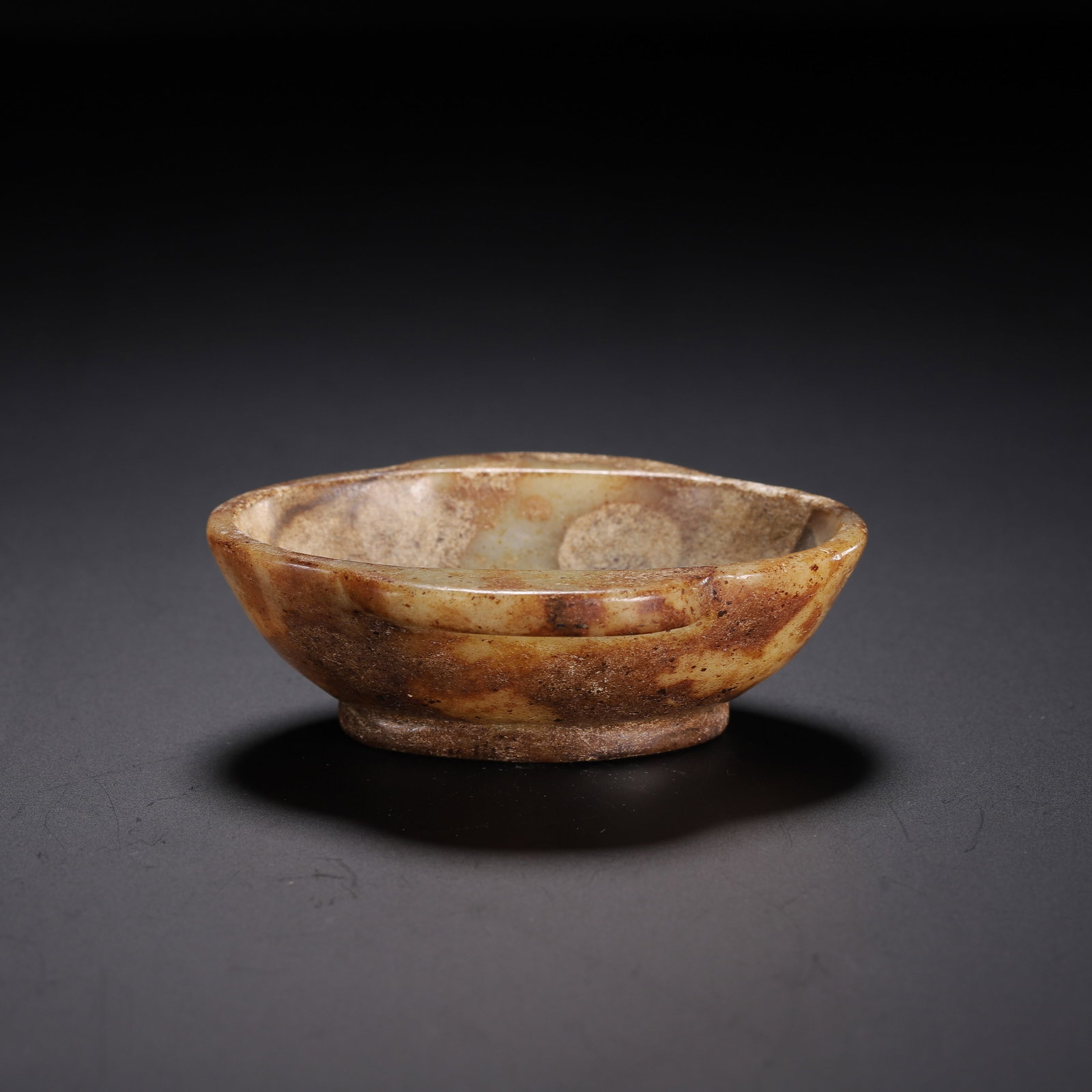 A CHINESE ARCHAIC JADE LOBED CUP: Dimensions:L. 8 cm. W. 6 cm. H. 2.5 cm. Weight 70 grams. A Chinese archaic jade lobed cup, carved from warm yellowish nephrite with natural russet and earthy patina, reflecting its ancient burial