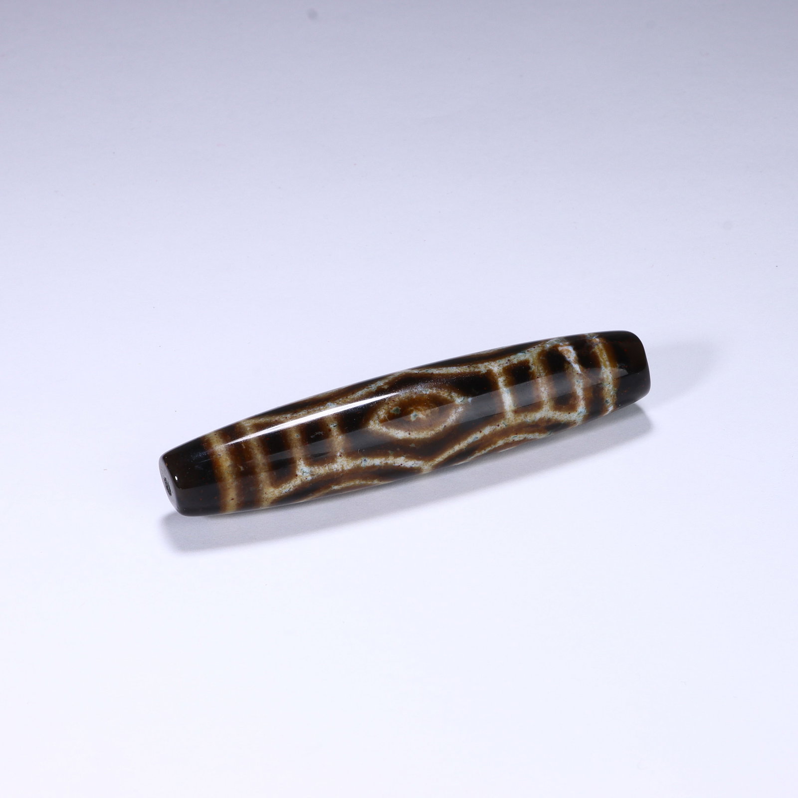 CHINESE BANDED AGATE DZI BEAD: Dimensions:L. 7.9 cm. A Chinese elongated Dzi bead, measuring 7.9 cm in length, featuring a deep brown base with creamy white geometric patterns. The bead displays a central mythical "eye" motif,