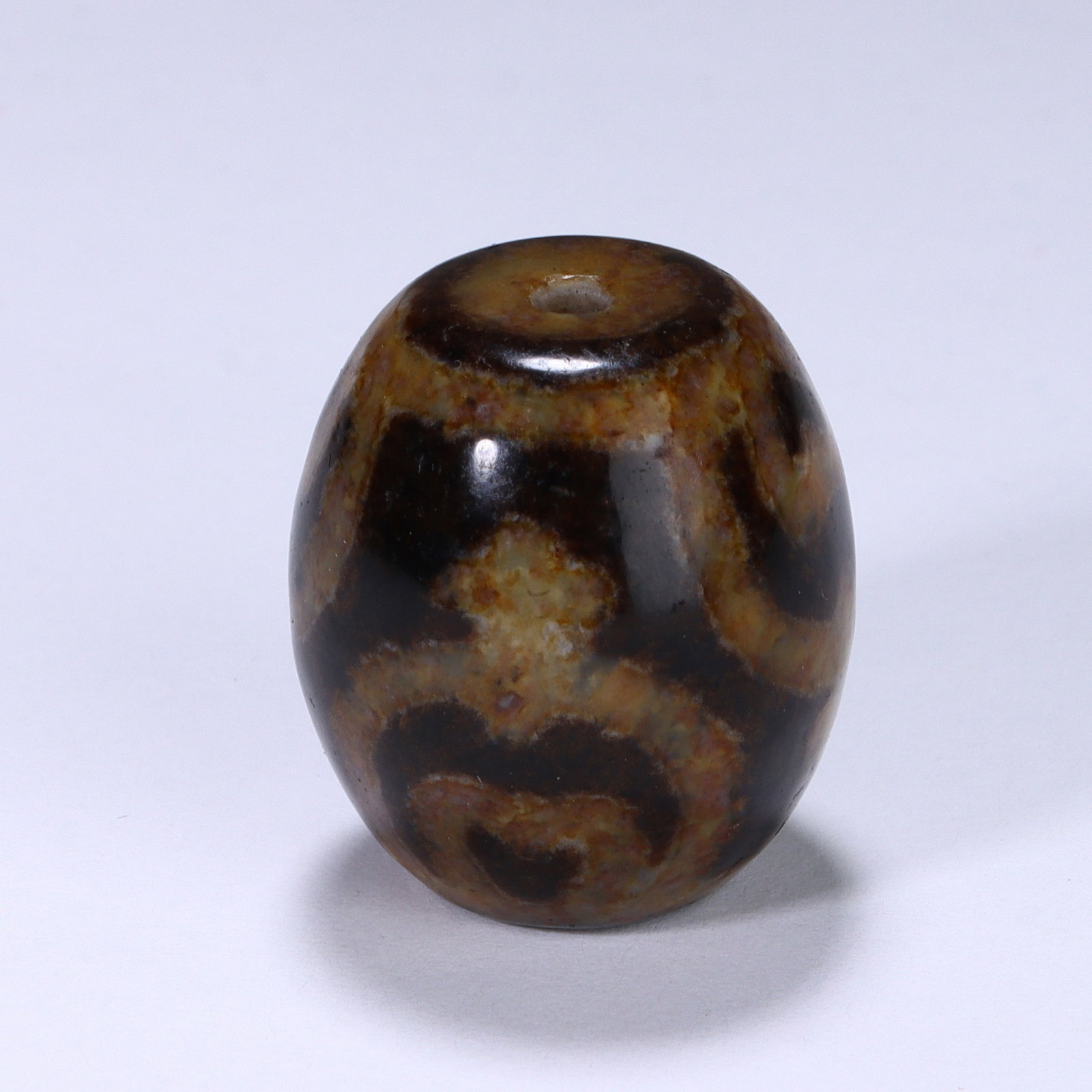 CHINESE BOTTLE GOURD MOTIF DZI BEAD: Dimensions:L. 2.2 cm. A Chinese oval Dzi bead, measuring 2.2 cm in length, crafted from polished agate with a warm earthy base. The bead features a central "bottle gourd" (hulu) motif in creamy