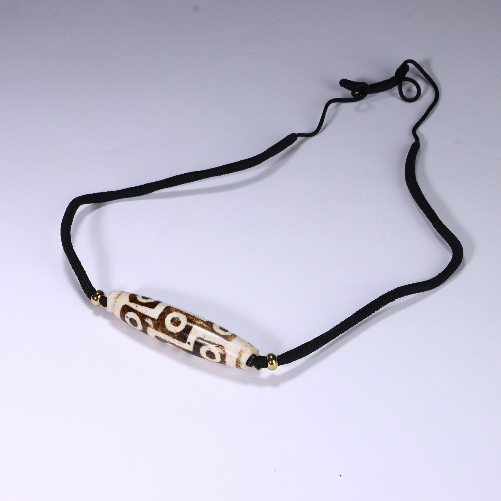 CHINESE NINE-EYE DZI BEAD NECKLACE: Dimensions:L. 5.8 cm. A Chinese Dzi bead necklace centered on a cylindrical Dzi bead measuring 5.8 cm in length, featuring a creamy ivory base with rich brown geometric patterns. The bead