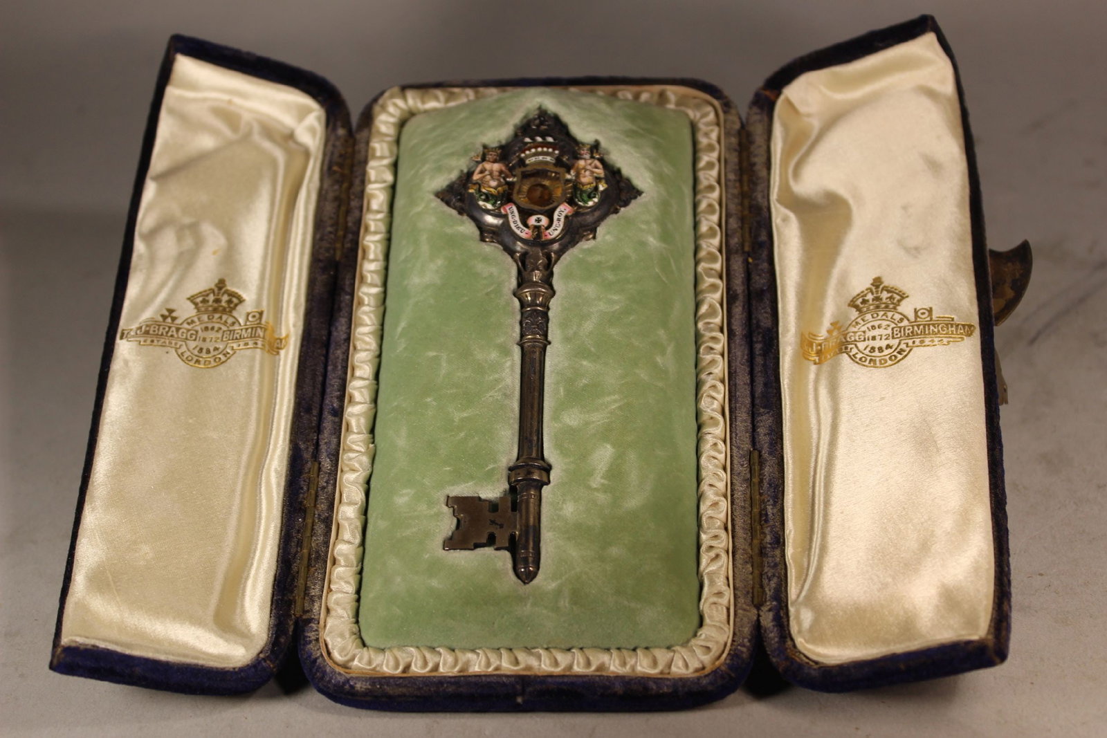 T&J BRAGG, LONDON, SILVER AND ENAMEL KEY AWARD IN PRESENTATION BOX, HAVING MERMEN, MISSING PEARL,: T&J BRAGG, LONDON, SILVER AND ENAMEL KEY AWARD IN PRESENTATION BOX, HAVING MERMEN, MISSING PEARL, KEY IS 5" x 2", VERY GOOD CONDITION.