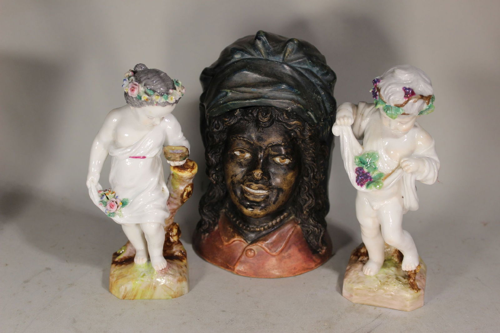 TERRACOTTA BLACKAMOOR HUMIDOR AND TWO EARLY CONTINENTAL PORCELAIN PUTTTI FIGURES HAVING CROSS SWORDS (1 of 5)