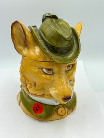 AN ANTIQUE SCHIERHOLZ PORCELAIN FOX BEER STEIN, 5.25" X 7" X 7". REPAIRS TO TOP, MISSING FEATHER.