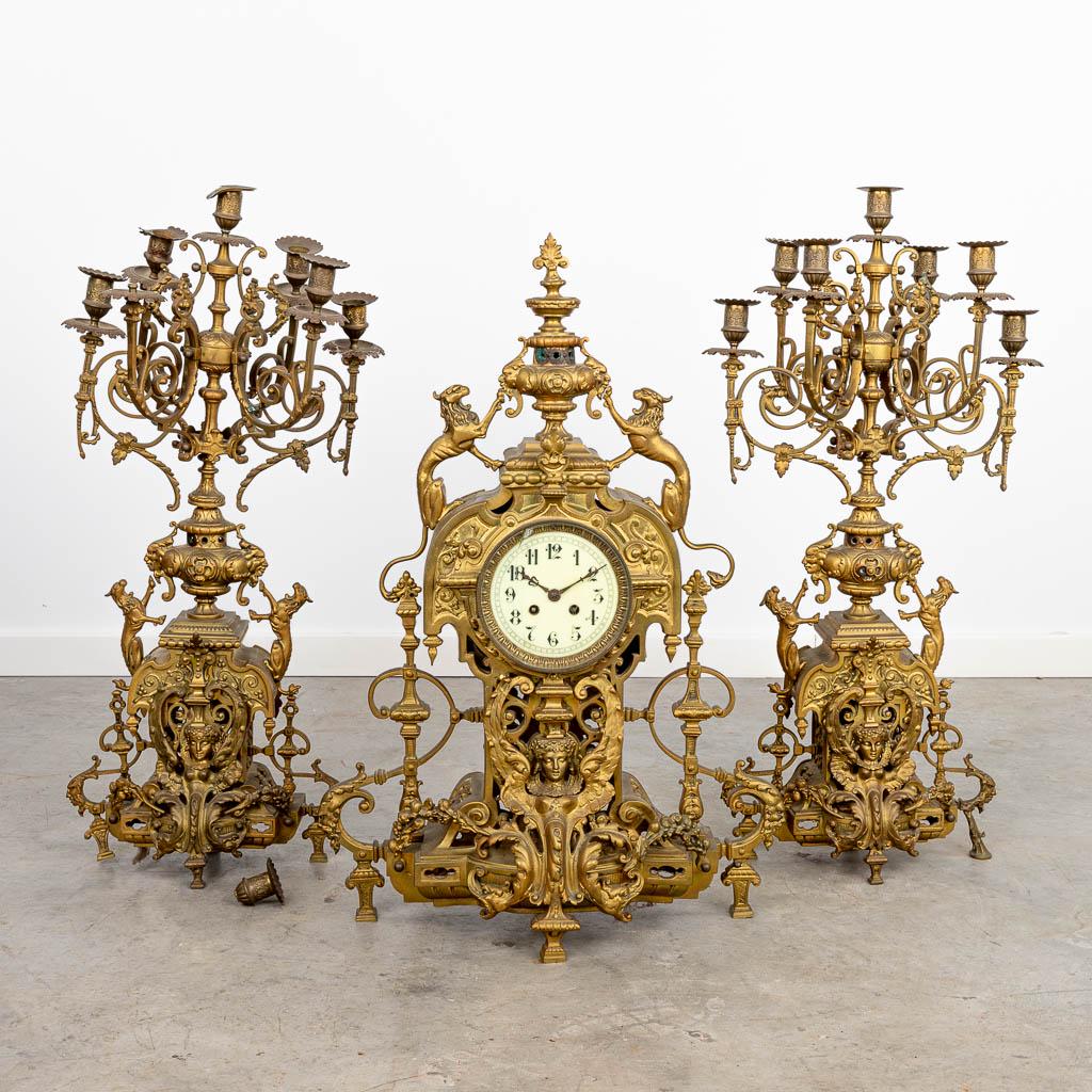 A three-piece mantle clock made of a bronze clock with: A three-piece mantle clock made of a bronze clock with candelabra. Candelabra height: 74 cm. (70 cm)
