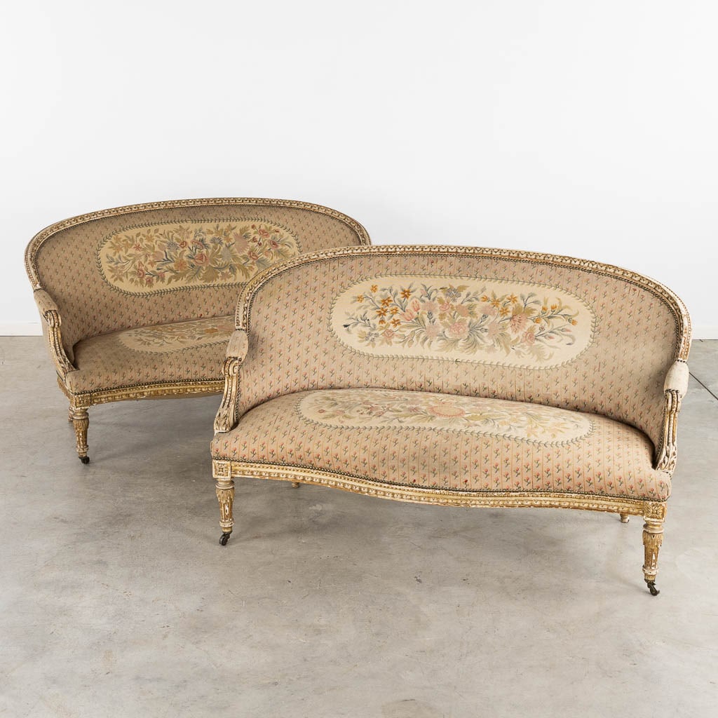 A pair of settees or sofas, sculptured wood in Louis XVI style, embroideries. Circa 1920. (L:80 x: A pair of settees or sofas, sculptured and gilt wood in Louis XVI style, further finished with embroideries and a floral decor. Circa 1920. Dimensions: (L:80 x W:150 x H:91 cm)