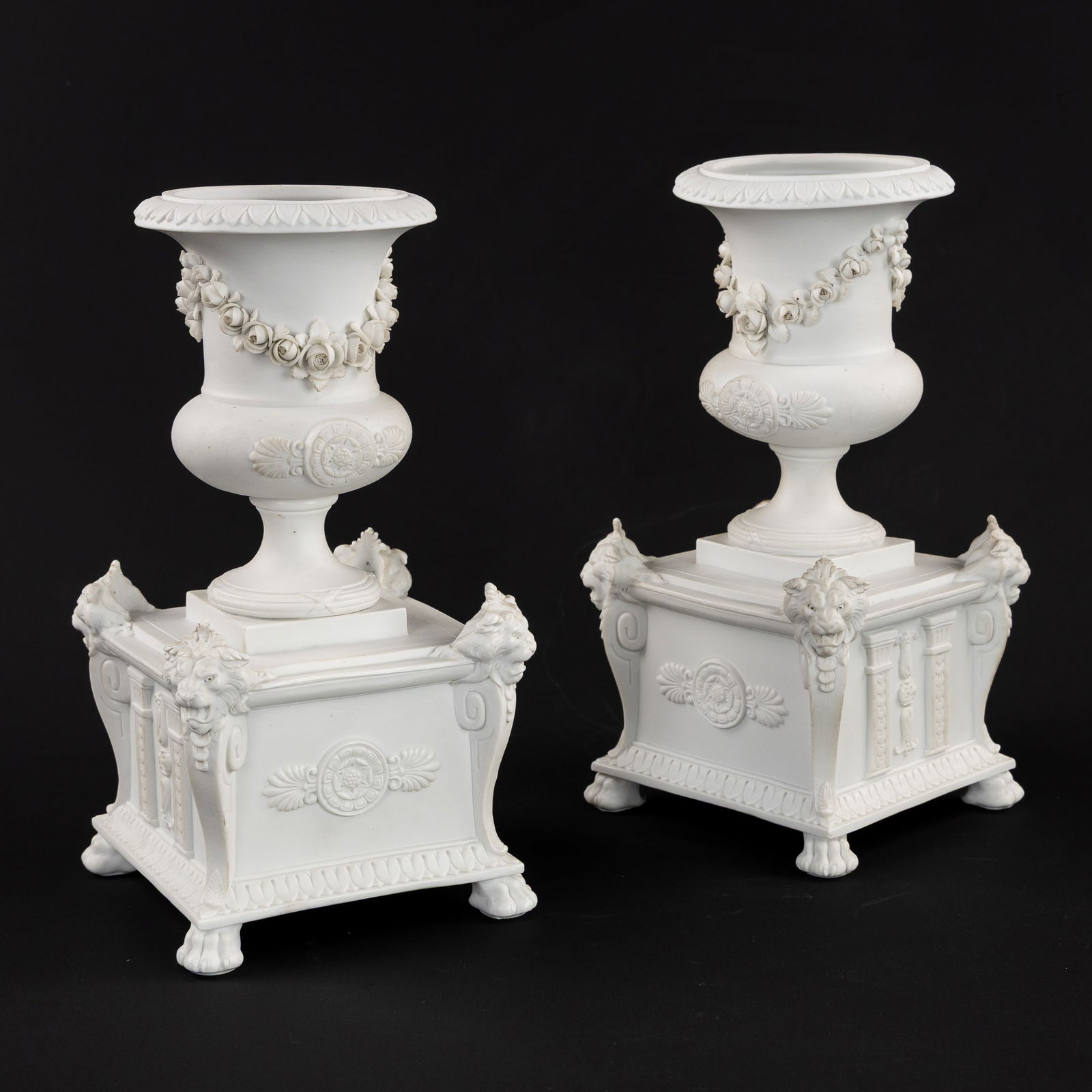 A Pair of Jardinieres or Urn Vases, with Lion Heads, Biscuit Porcelain, Neoclassical style.: A Pair of Jardinieres or Urn Vases, with Lion Heads, Biscuit Porcelain, Neoclassical style. Biscuit porcelain.Urn vases mounted on a square base.Decorated with lion heads, garlands, and palmette frame