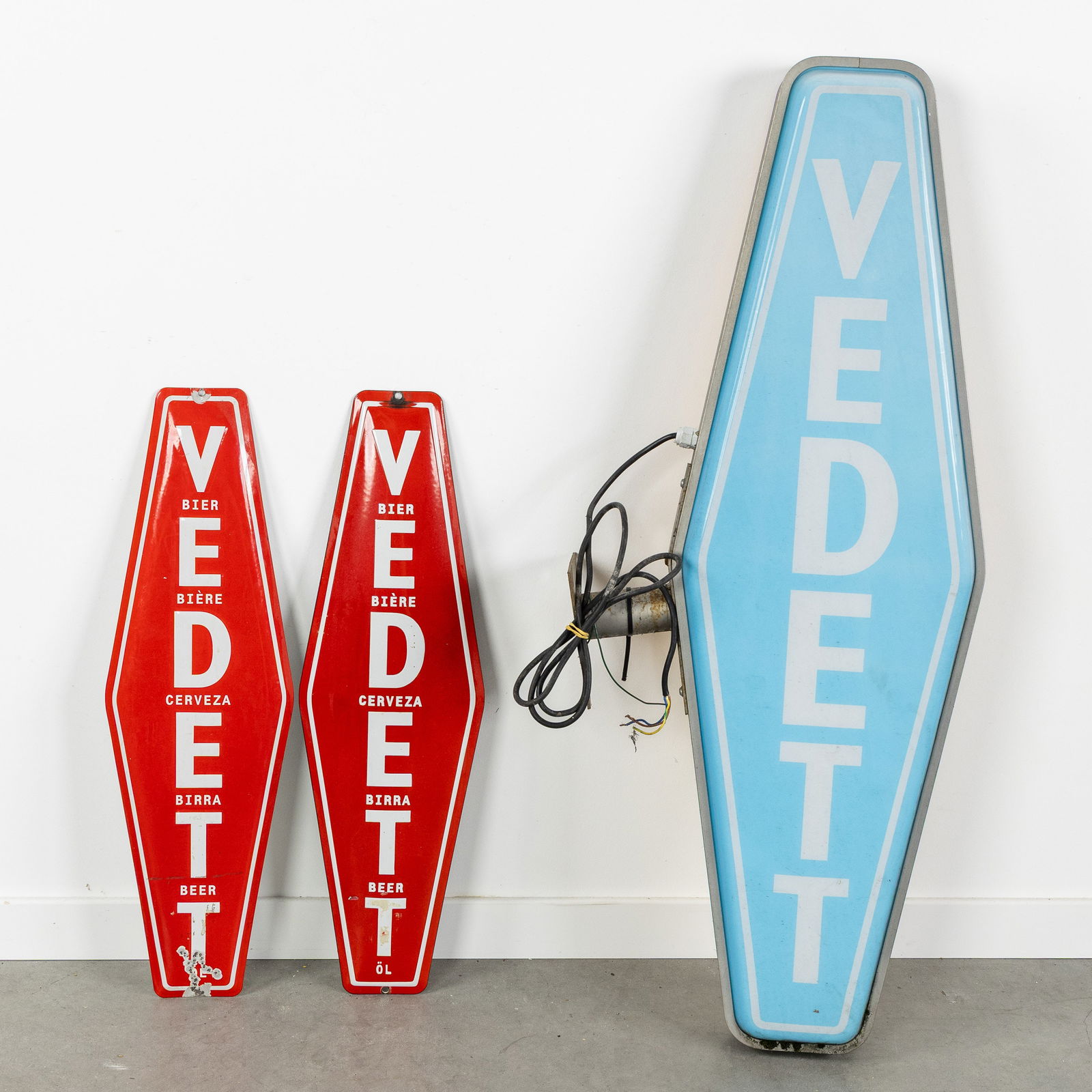 Two enamel advertising signs and a light board, 'Vedett'.: Two enamel advertising signs and a light board, 'Vedett'. Enamel advertising signs. Vedette, Beer - Bière - Cerveza - Birra - Beer (2x) (65 x 20 cm). Light board, plexiglass and metal. Vedette, yello