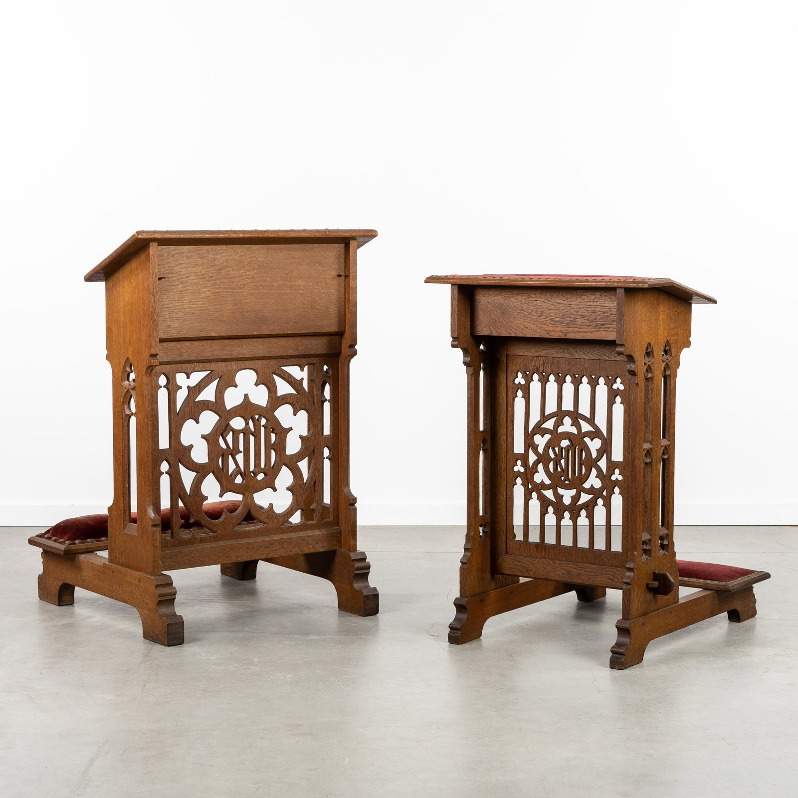 Two Gothic Revival prayer benches, carved with openwork and upholstered in red velvet.: Two Gothic Revival prayer benches, carved with openwork and upholstered in red velvet. Sculptured wood, upholstered in red velvet.Decorated with Gothic framework and IHS monogram.