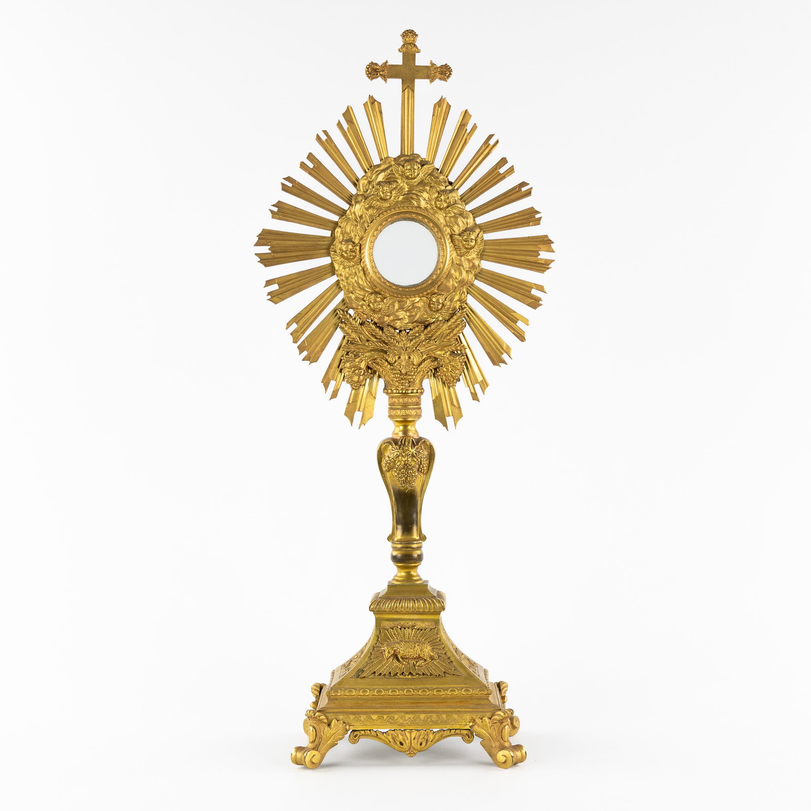 A Brass Sunburst Monstrance with Angel heads and the Lamb of God, Baroque style.: A Brass Sunburst Monstrance with Angel heads and the Lamb of God, Baroque style. Brass and bronze. Sunburst monstrance mounted with a crucifix. Decorated with angel heads, bunches of grapes and ears o
