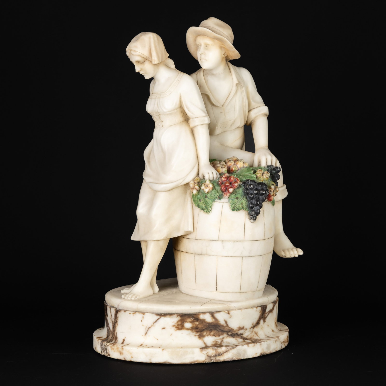 'After the Grape Harvest', a figurine, sculptured and patinated alabaster, circa 1900.: 'After the Grape Harvest', a figurine, sculptured and patinated alabaster, circa 1900. Sculptured and patinated alabaster, mounted on a marble base.Depiction of a young couple on a wine barrel, covere