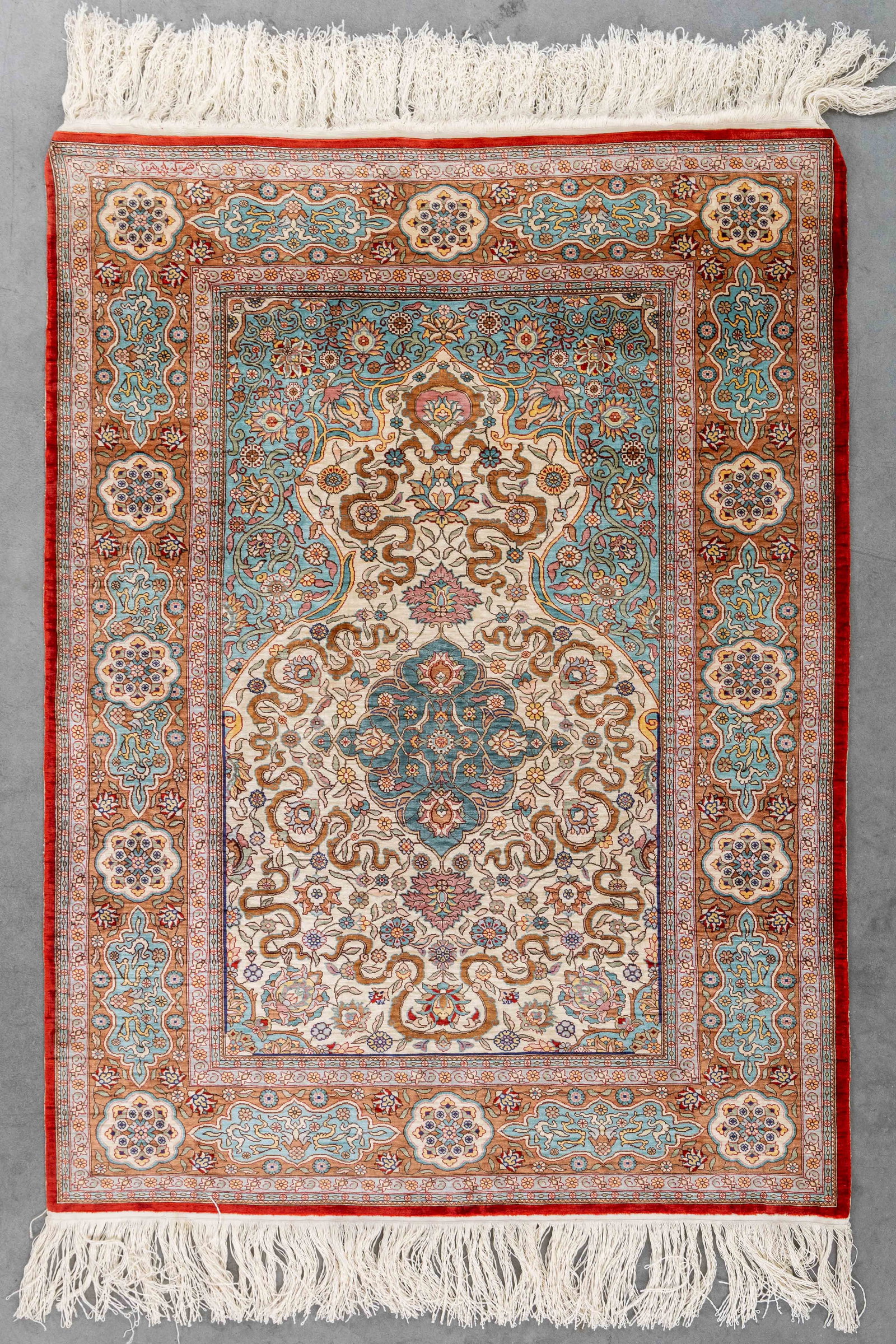 An Oriental hand-made carpet, Silk, Hereke, Turkiye (99 x 74 cm).: An Oriental hand-made carpet, Silk, Hereke, Turkiye (99 x 74 cm). Signed. Dimensions: (W:74 x H:99 cm) The absence of a condition report does not imply a perfect item. Please send us an e-mail to requ