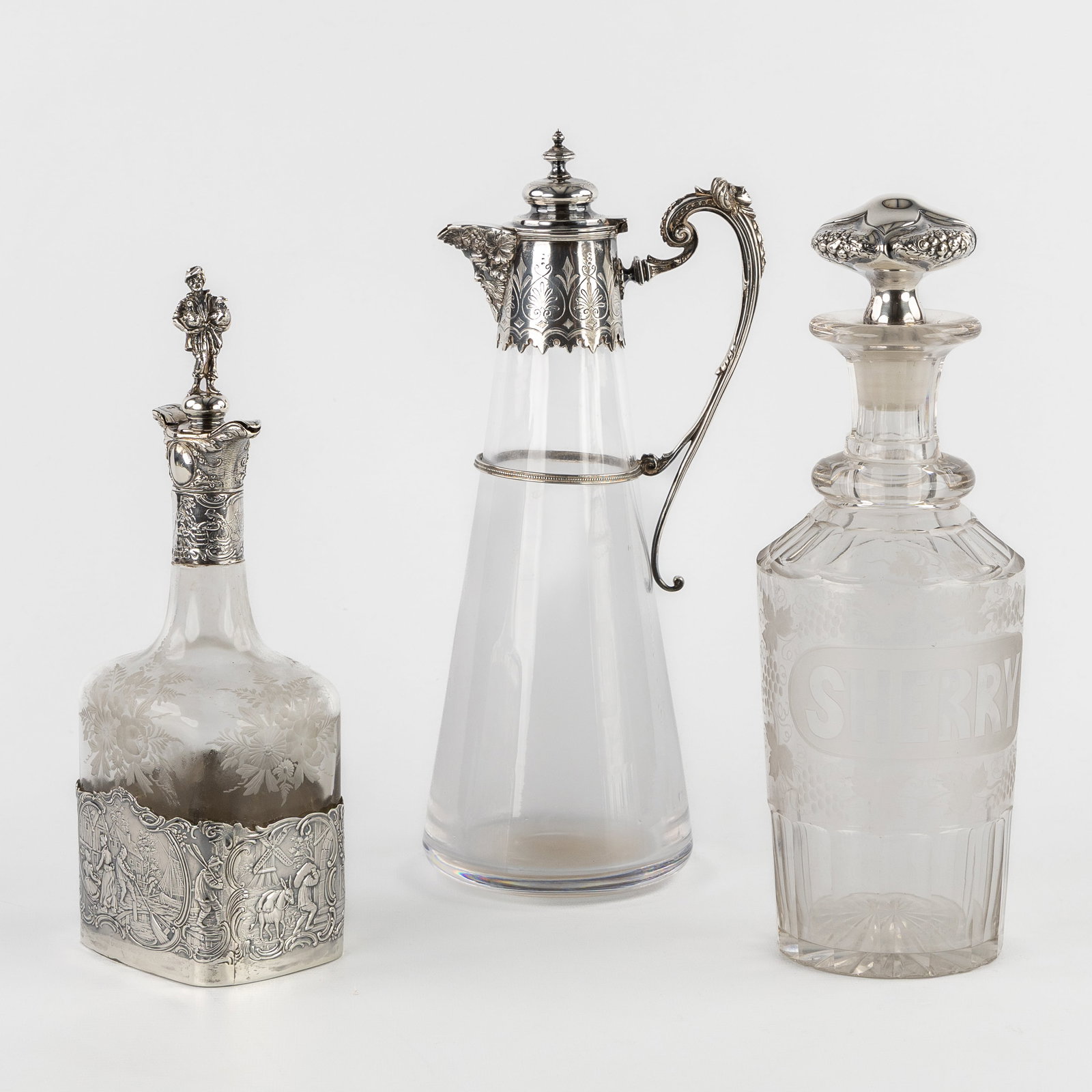 A Collection of three crystal carafes or decanters with silver mounts. England and Germany, 19th and: A Collection of three crystal carafes or decanters with silver mounts. England and Germany, 19th and early 20th century. A sherry carafe, cut and etched/engraved crystal, with a silver-mounted stopper