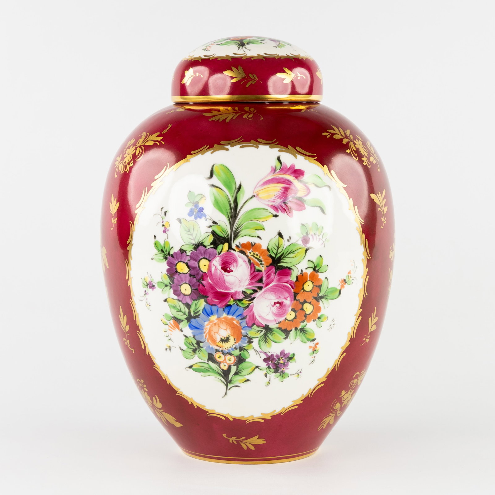 Limoges, a large porcelain covered vase with hand-painted floral decoration, France, 20th C.: Limoges, a large porcelain lidded vase with hand-painted floral decoration, France, 20th century. Polychrome porcelain, burgundy ground.Decorated with hand-painted floral motifs, with gilded finish.