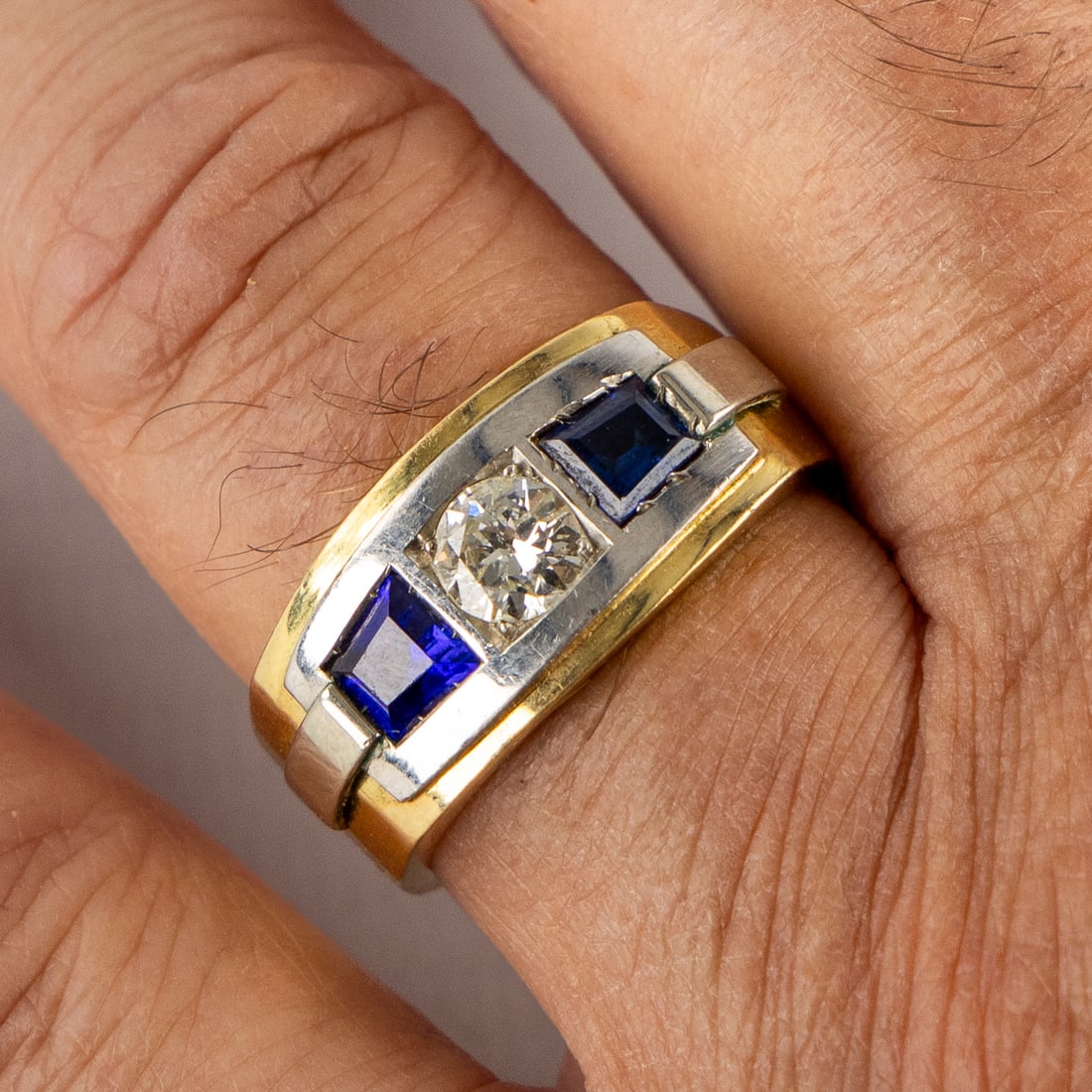 Een ring, 18kt geel goud gemonteerd met een briljant, circa 0,7 ct en 2 saffieren. 15,93g.: A ring in 18-carat yellow and white gold, set with one diamond and two sapphires. Ring size 67, 15.92g. Set with a large brilliant-cut diamond of approximately 0.7ct.Flanked by two sapphires.