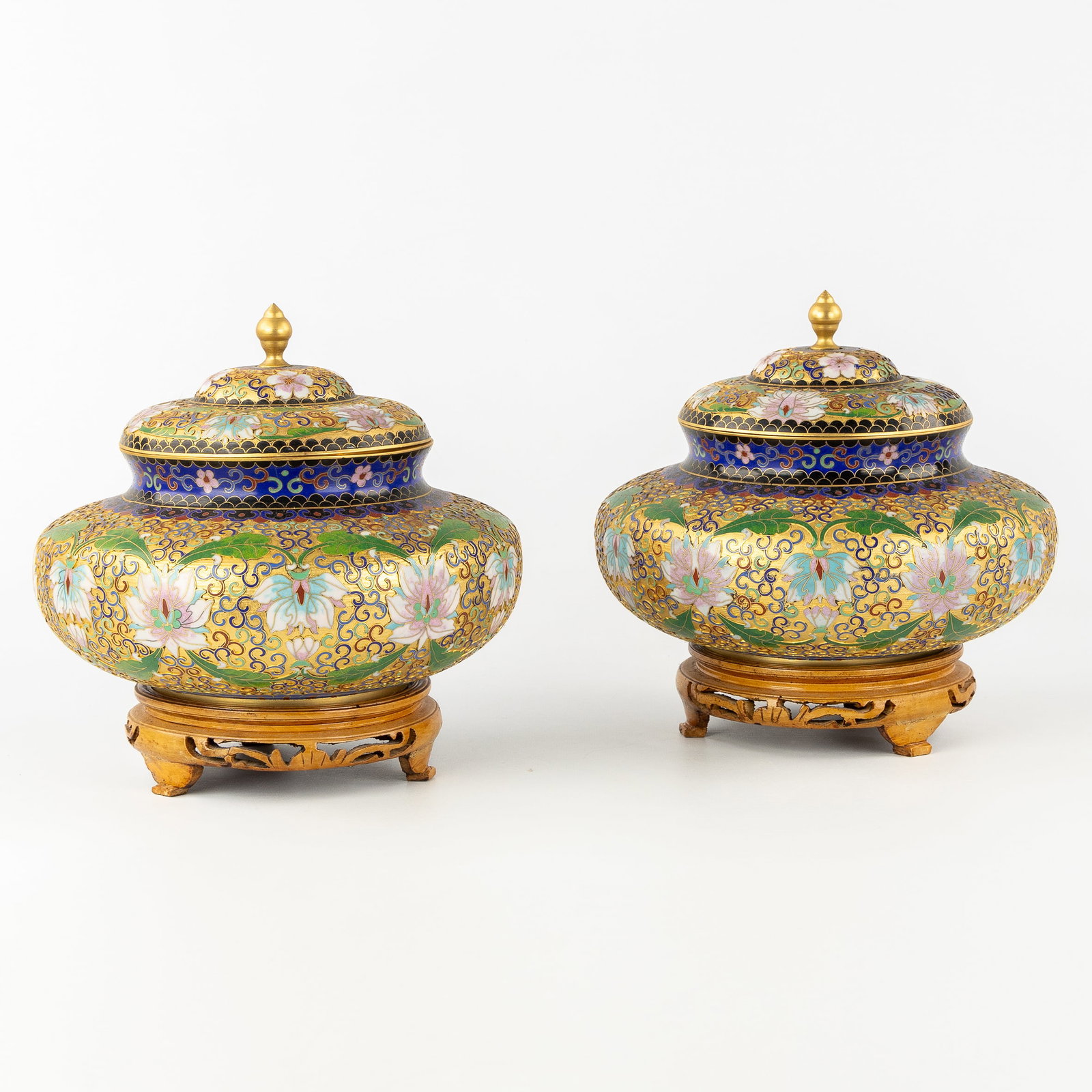 A Pair of Oriental Cloisonné lidded bowls with a floral decoration. 20th C.: A Pair of Oriental Cloisonné lidded bowls with a floral decoration. 20th century. Richly decorated with peonies and leaf motifs.With wooden bases/stands and original box.20th century.