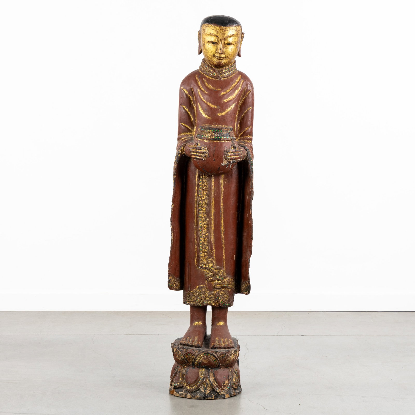 A Decorative statue of a Burmese Monk with an Alms bowl, sculptured and gilded wood.: A Decorative statue of a Burmese Monk with an Alms bowl, sculptured and gilded wood. Sculptured, patinated, and gilded wood.Burmese monk with an alms bowl, standing on a Lotus throne.Finished with f