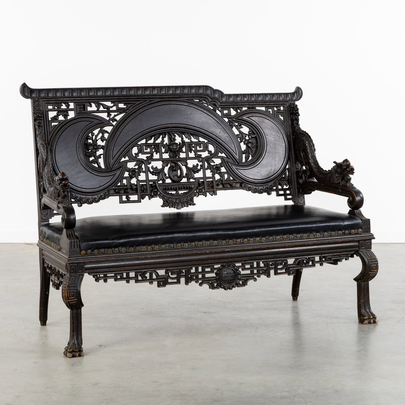 A Wood-sculptured Chinese bench, richly decorated with dragons and openwork carving, circa 1900.: A Wood-sculptured Chinese bench, richly decorated with dragons and openwork carving, circa 1900. Sculptured and ebonized wood.Decorated with floral openwork carving, crescent moons, and sculptured dra