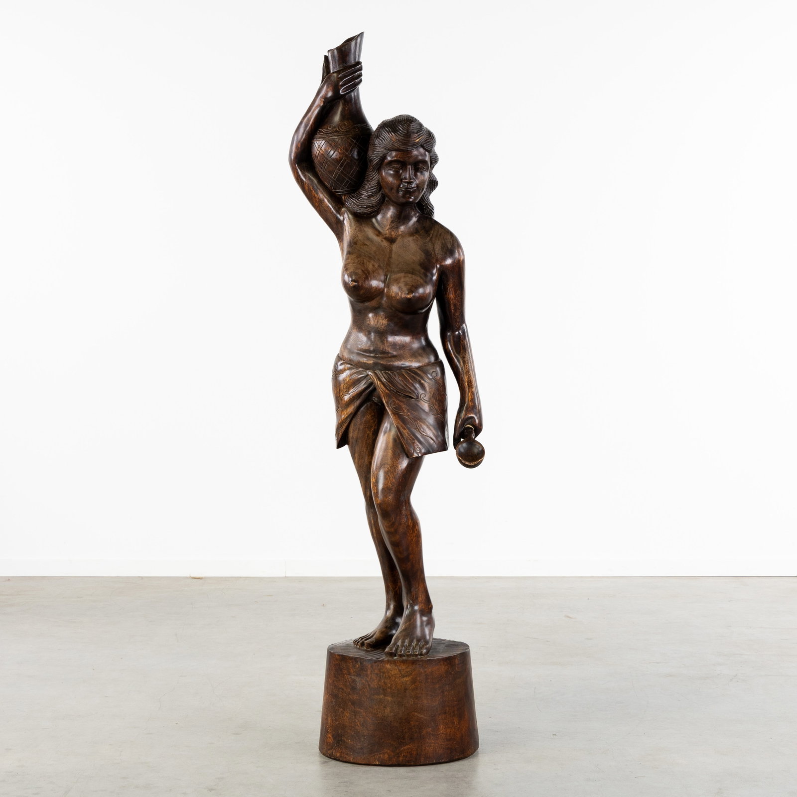 A Large decorative sculpture of a Lady with a Jug, sculptured wood, circa 1960.: A Large decorative sculpture of a Lady with a Jug, sculptured wood, circa 1960. Sculptured wood.Depiction of a half-naked lady with a jug on her shoulder and a spoon in her hand. (46 x 182 x 40 cm)