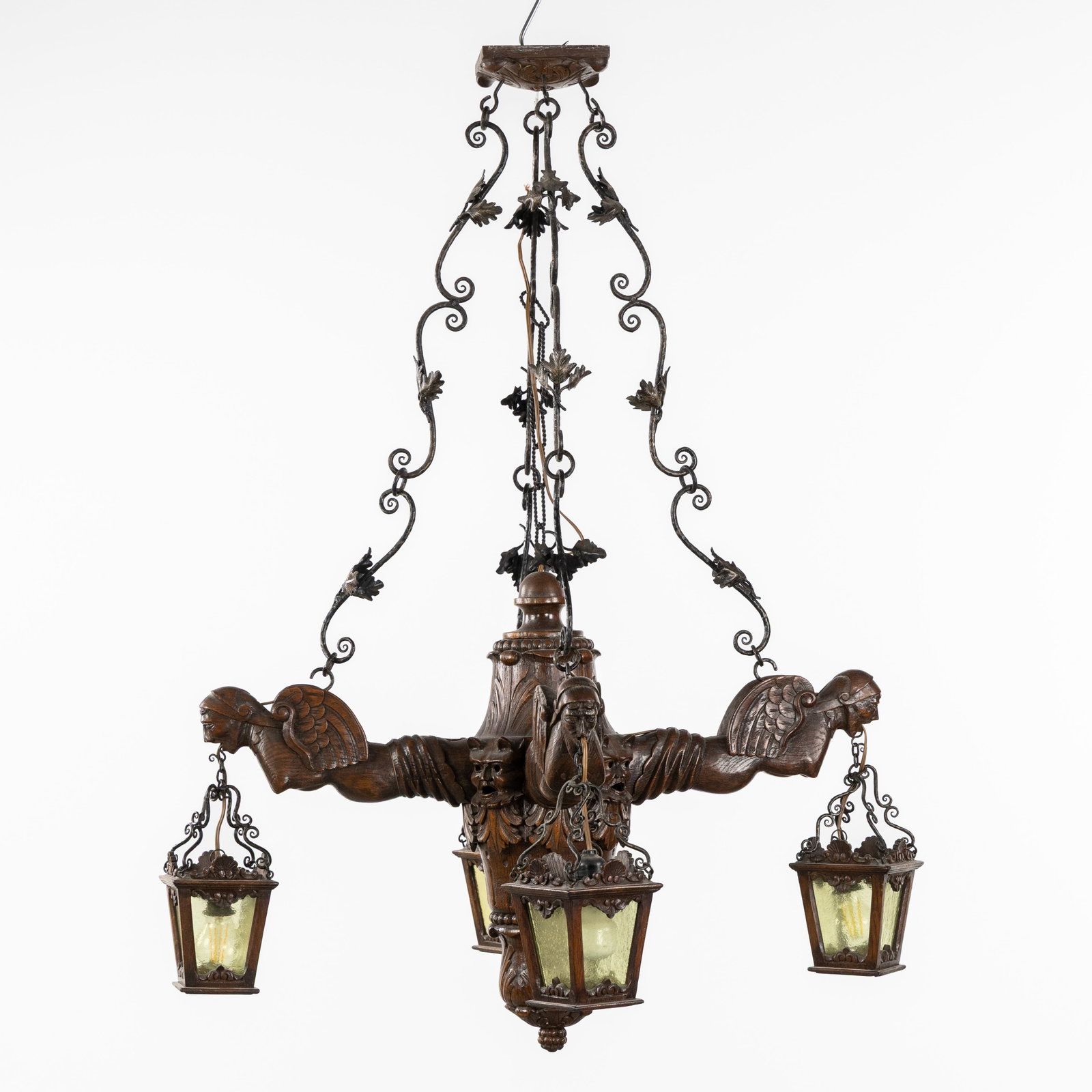 A Large, wood-sculptured chandelier with gargoyles and lanterns, circa 1900.: A Large, wood-sculptured chandelier with gargoyles and lanterns, circa 1900. Sculptured wood, wrought iron, and glass.Decorated with carved winged gargoyles.With four lanterns and a central light (l