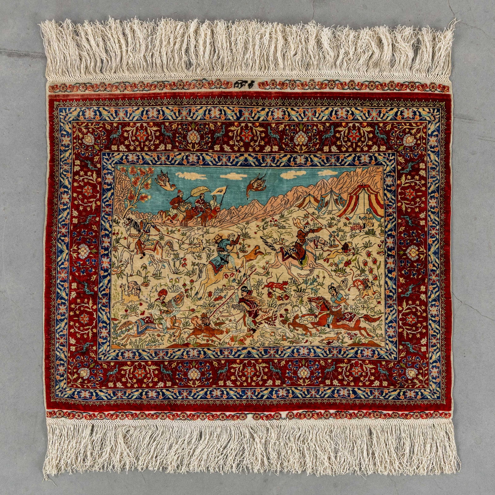 A Small Oriental very fine hand-made carpet with a hunting scene, 20/20, Silk, Ozipek, Hereke,: A Small Oriental very fine hand-made carpet with a hunting scene, 20/20, Silk, Ozipek, Hereke, Turkiye, signed (48 x 61 cm). Extremely fine hand-knotted (20 by 20 knots per cm²).With a hunting sc