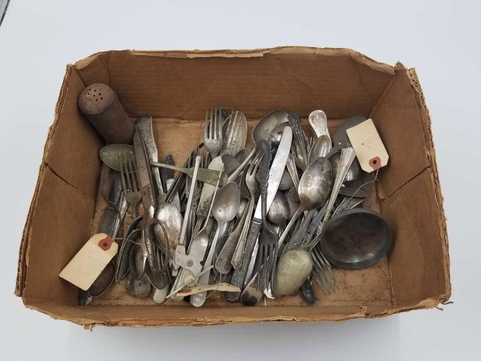 Box lot of Silverware: Box lot of early kitchen goods which include silverware, a Sheffield England spoon, sugar spoon, gravy ladle, an original Rogers scissors, can opener, and salt shaker. Several items are silver plated.