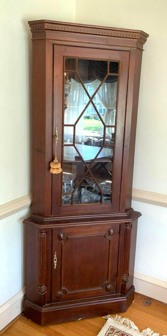 Mahogany Corner Cabinet: Mahogany corner cabinet with a glass front door containing two shelves for storage. The lower compartment contains one shelf and has carved columns and seashells on the door. It measures approximately