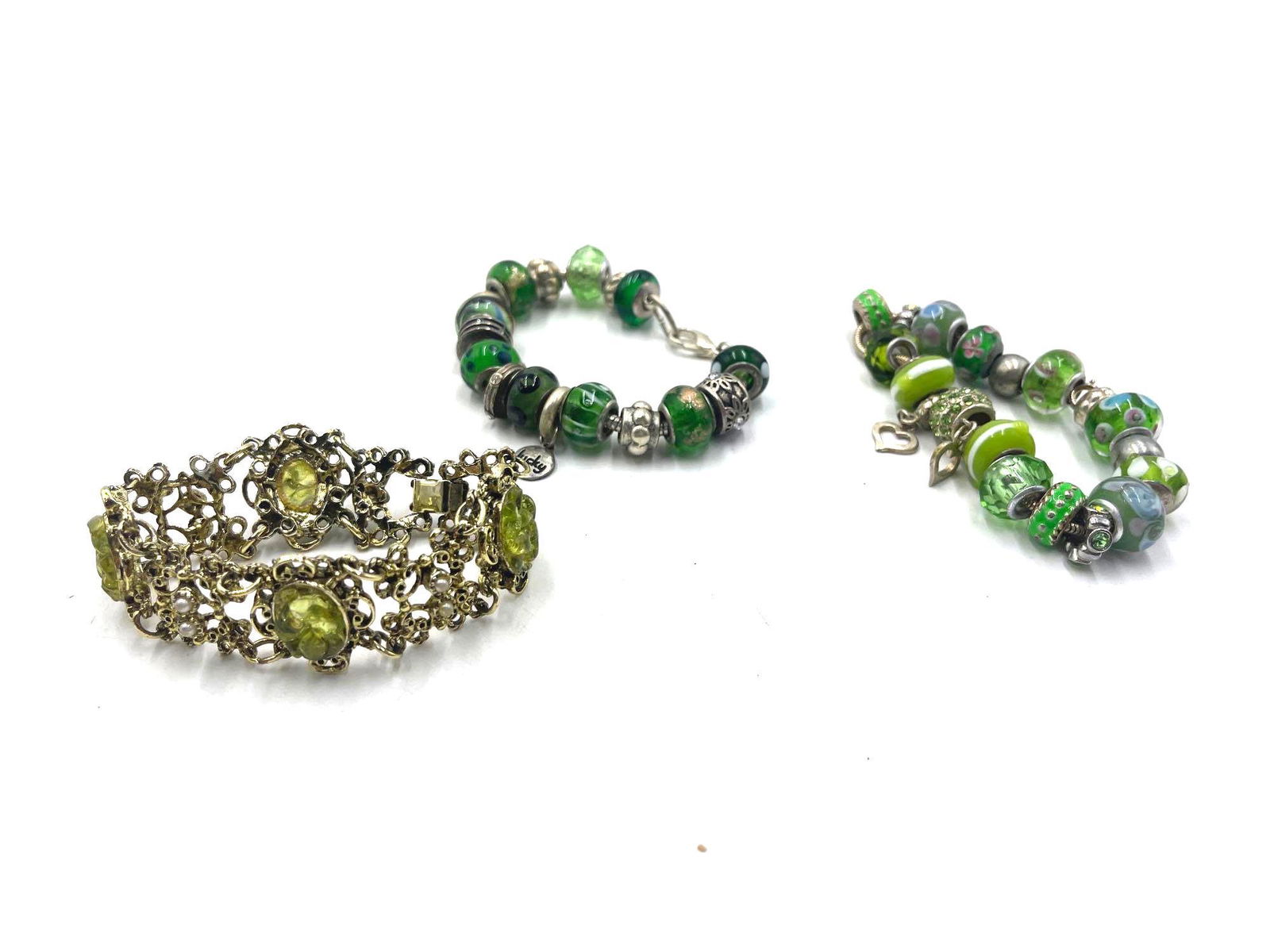 Assorted Green Bracelets: Collection of three bracelets, all of which sport a green theme. Of the three, two are beaded charm bracelets, and one is a gold tone metal chain bracelet with four green resin stones. All three brace