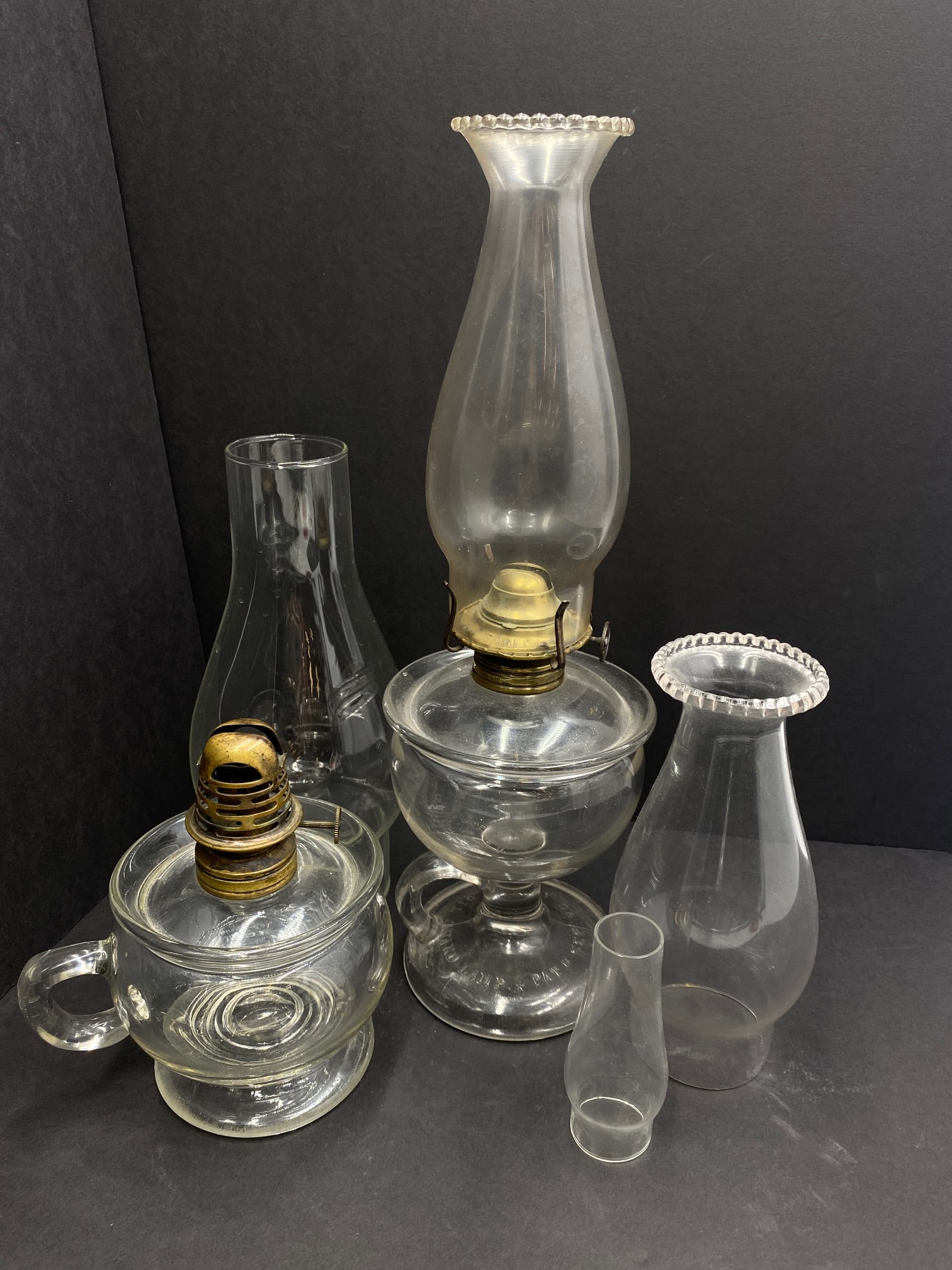 Vintage Oil Lamps and Assorted Glass Chimneys: Vintage Oil Lamps: Taller of the two oil lamps measures 13" from base of lamp to tip of chimney. Marked PAT Sep 20 1870 on base of glass pedestal. Holds a 2" chimney. Wick knob reads "Made in US" Eagl