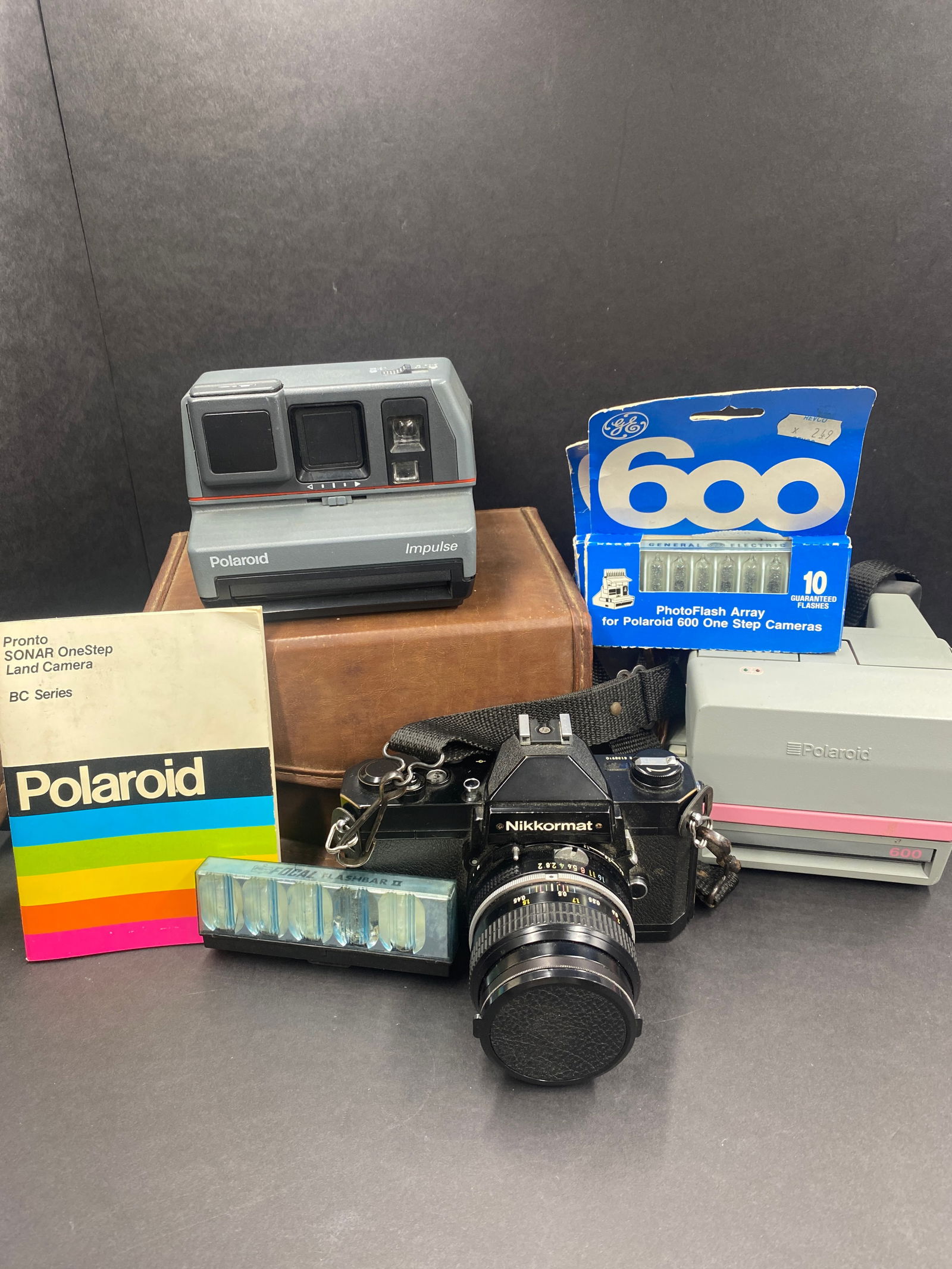 Assorted Cameras including Polaroid and Nikon: Assorted Cameras including 2 Polaroids and one Nikon: Nikon Camera has a Nikkor 50mm 1:2 attached lens f2.8 - f16. Polaroid Impulse has a flash and carry case. The pink and gray Polaroid is Cool Cam 6
