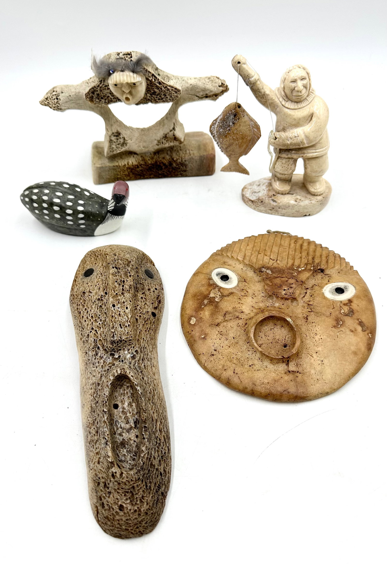 Bone and Stone Carved Inuit Figurines: Bone and Stone Carved Inuit Figurines. Includes a long bone mask carved figure with an open mouth, and a round mask. It also includes a carved bone vertebrae figure with a carved face and feathers. It
