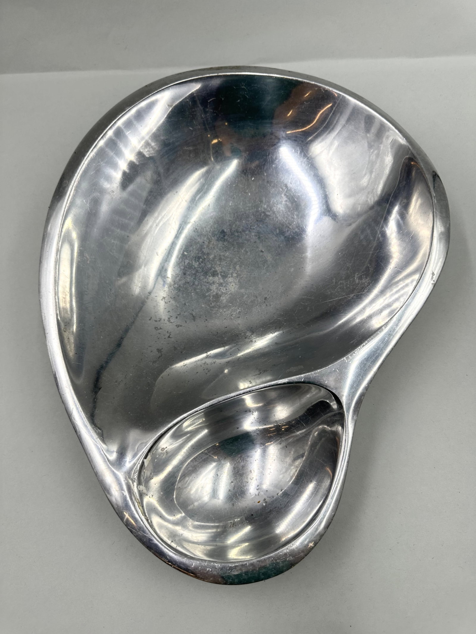 1980s Nambe' Steel Shrimp and Sauce Bowl: Nambe' shrimp and sauce bowl made of steel. The bowl is in an organic shape. The bottom of the bow is stamped Nambe' 560. Measures 14.5x10.5in An in-person inspection is available for all auctions. Bl