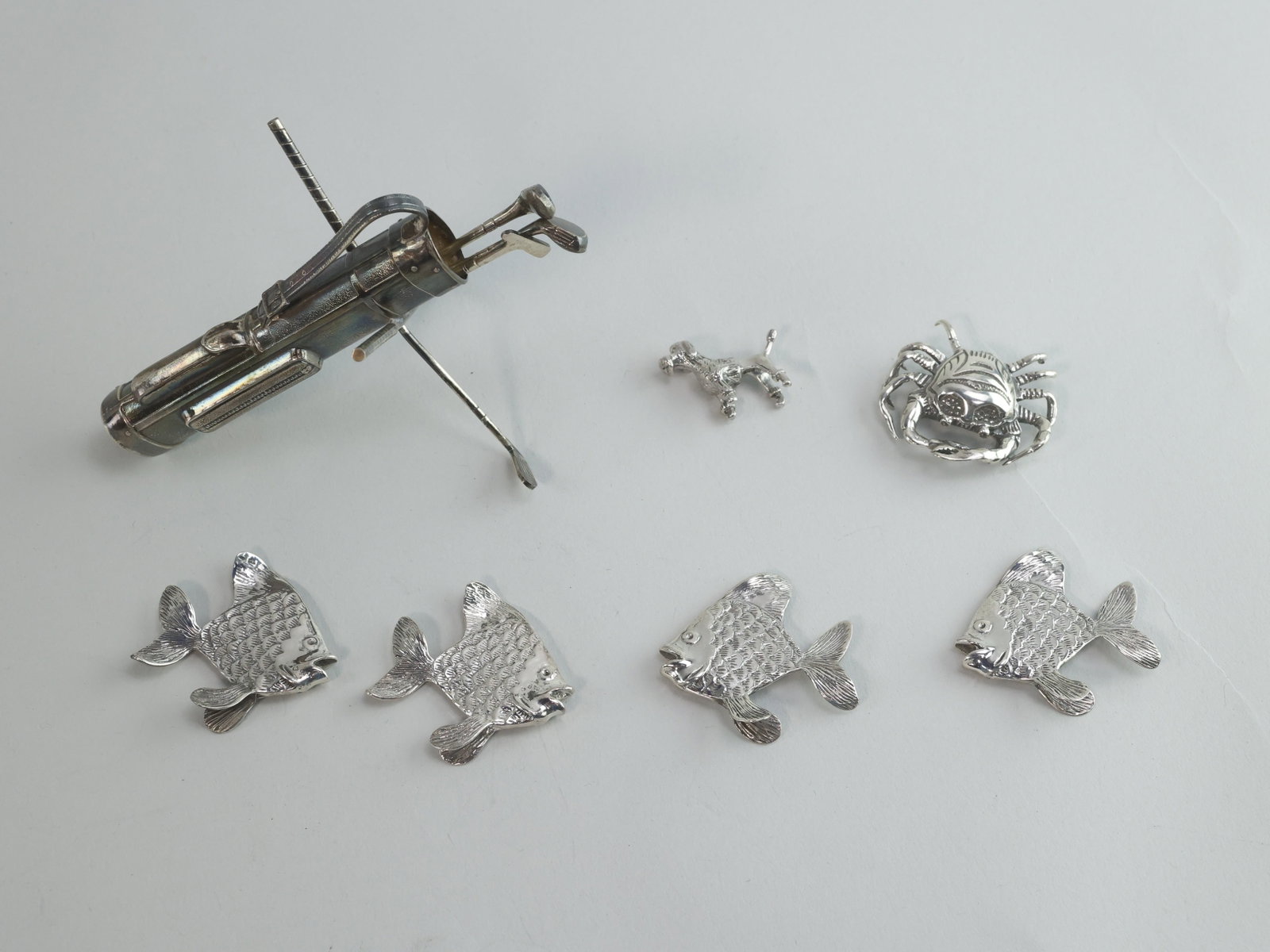 925 Sterling Silver Figurines and Cocktail Forks: Seven sterling silver figurines in total. Four of the figurines are fish that stand on their fins. The scales and other details are etched into the body. Below the open mouth, the fish are marked 925.