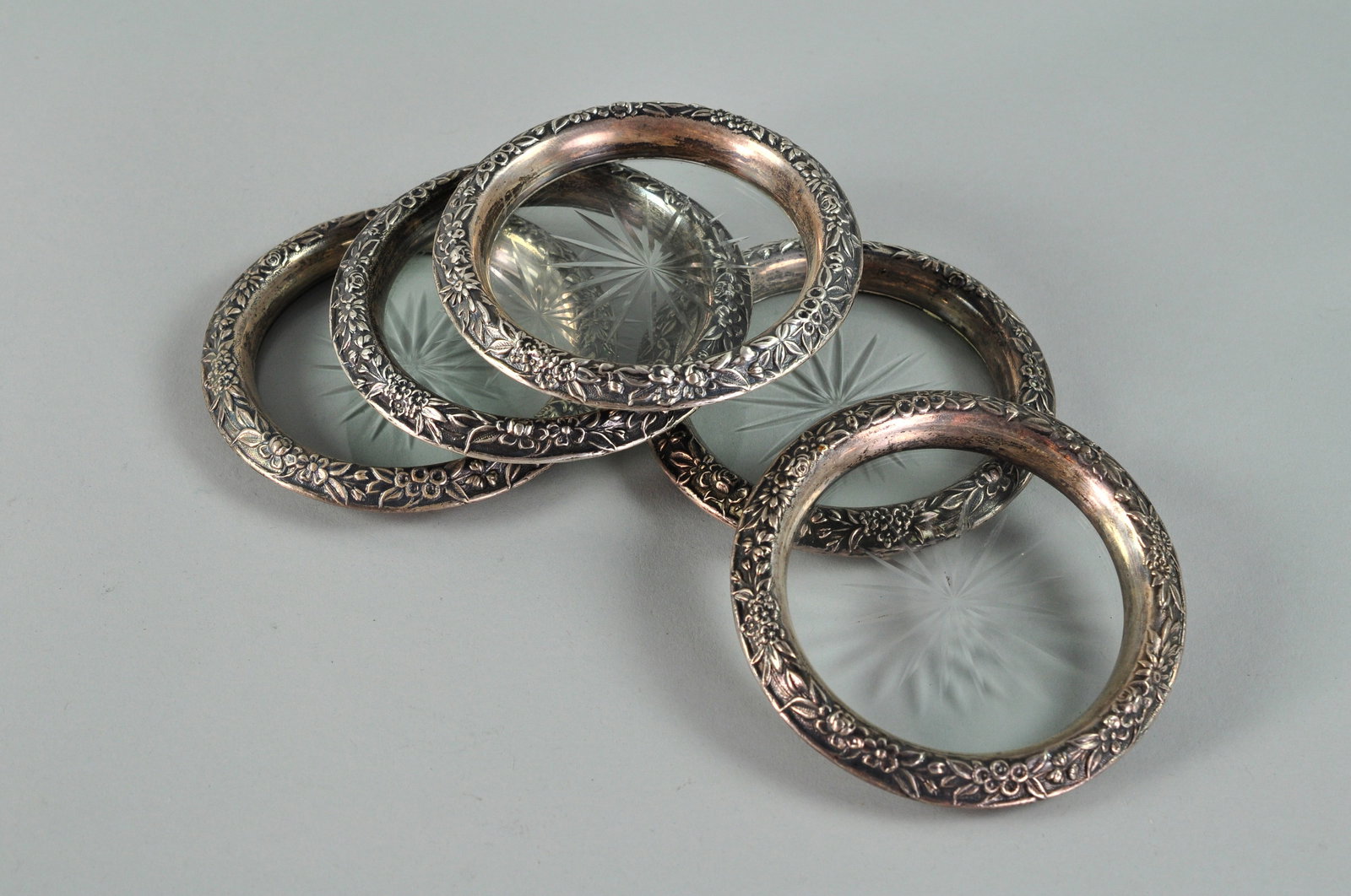 Crystal Coasters with Sterling Silver Rim: Five crystal coasters with sterling silver rims decorated with a floral organic design created by Kirk and Son. The metalwork technique is called repousse where the silver is hammered from behind to c