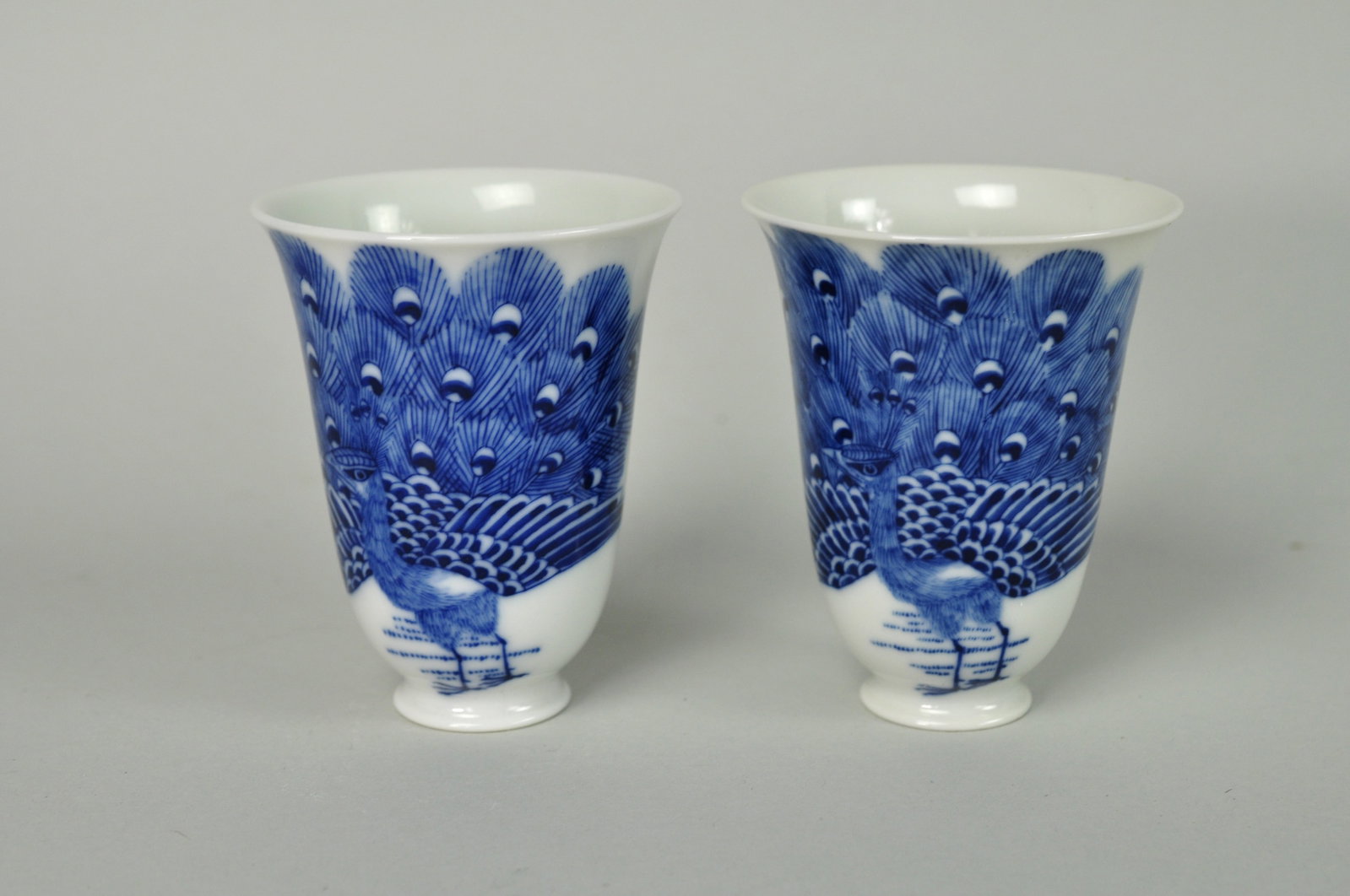 Chinese Peacock Porcelain Wine Cups 20th Century: Two 20th Century Chinese porcelain blue and white wine cups decorated with a peacock with their train open. The wine cups show no visible ch