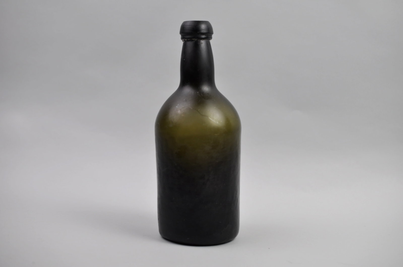 Mallet Bottle from 18th Century: Dimensions: Approx 1/2x3 1/2x9 3/4" Condition: Contains Scratches, Hairline Cracks, and Chipping Additional Information: This turn-mold black glass liquor bottle is fine example of ut