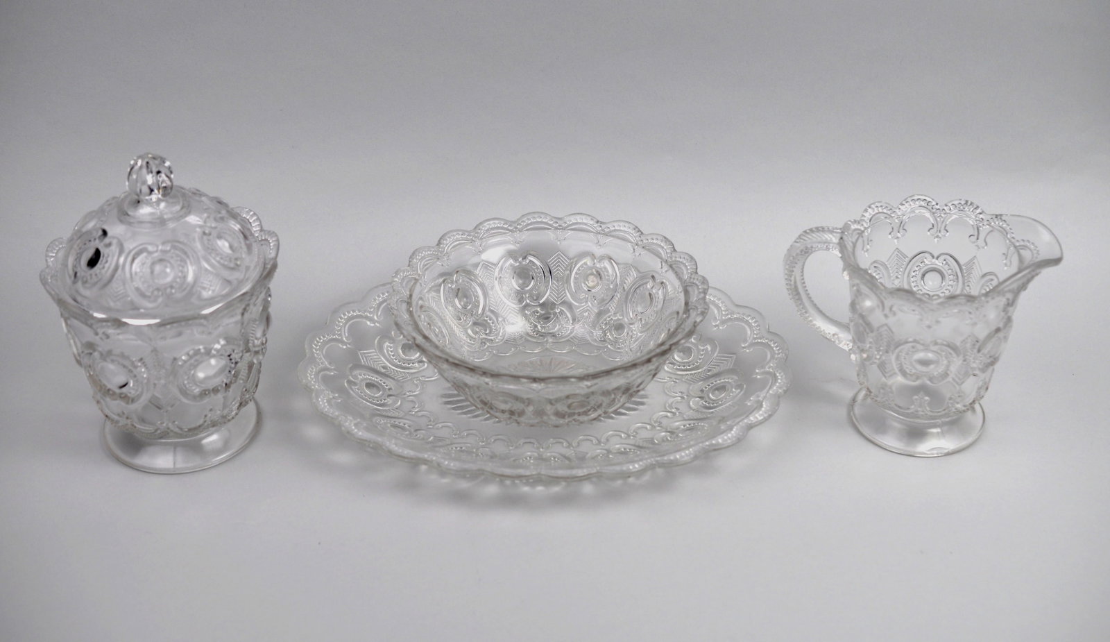 Tennessee Pressed Glass Collection: Manufacturer: U.S. Glass Co. Dimensions: Various Condition: Candy Dish has a Broken Tip and a Vertical Crack Additional Information: This four-piece collection from American Glass Co. features the