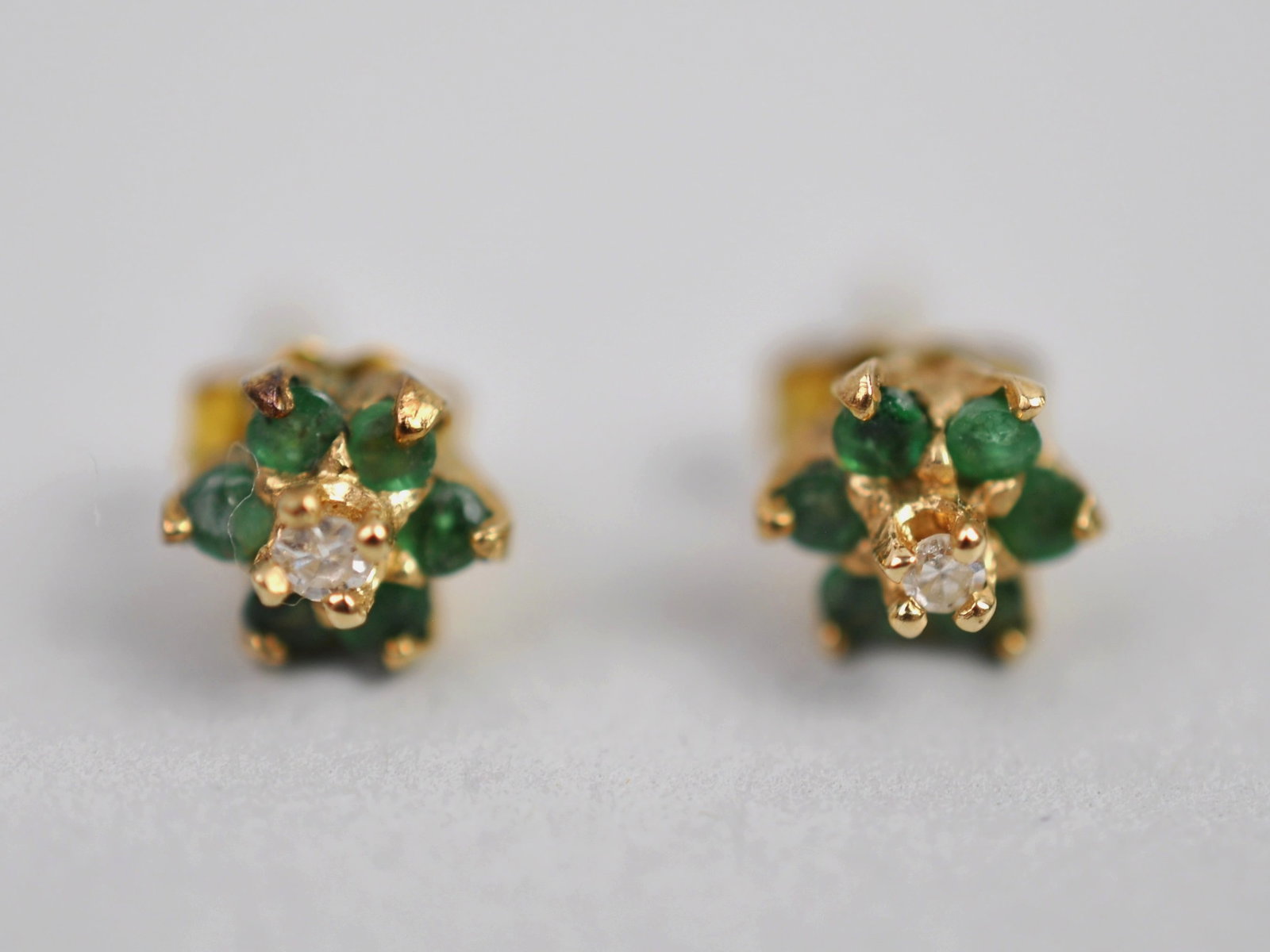 14K Gold Diamond & Emerald Stud Earrings: Metal: 14K Yellow Gold Stone Types: Emerald, Diamond Dimensions: Approx. 5mm Cluster Weight: Approx. 0.04ozt Condition: No Visible Flaws Additional Information: Pair of 14K yellow gold flower cluster