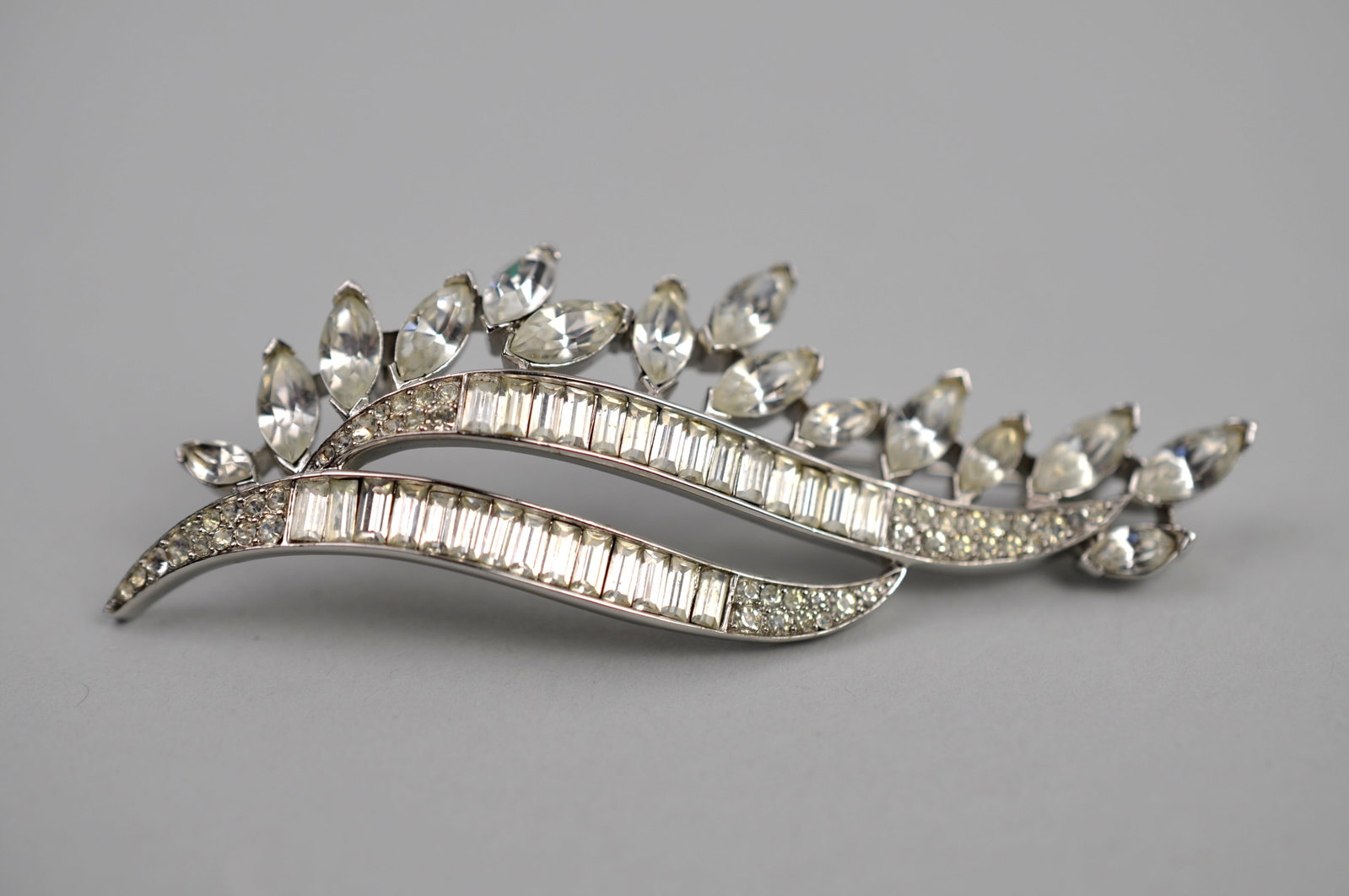 Trifari Rhodium-Plated Rhinestone Brooch: Metal: Rhodium-Plated Base Metal Stone Types: Clear Rhinestones Dimensions: Approximately 3 in. long Weight: 0.60ozt Condition: No visible flaws. Additional Information: Signed Trifari rhodium-plated