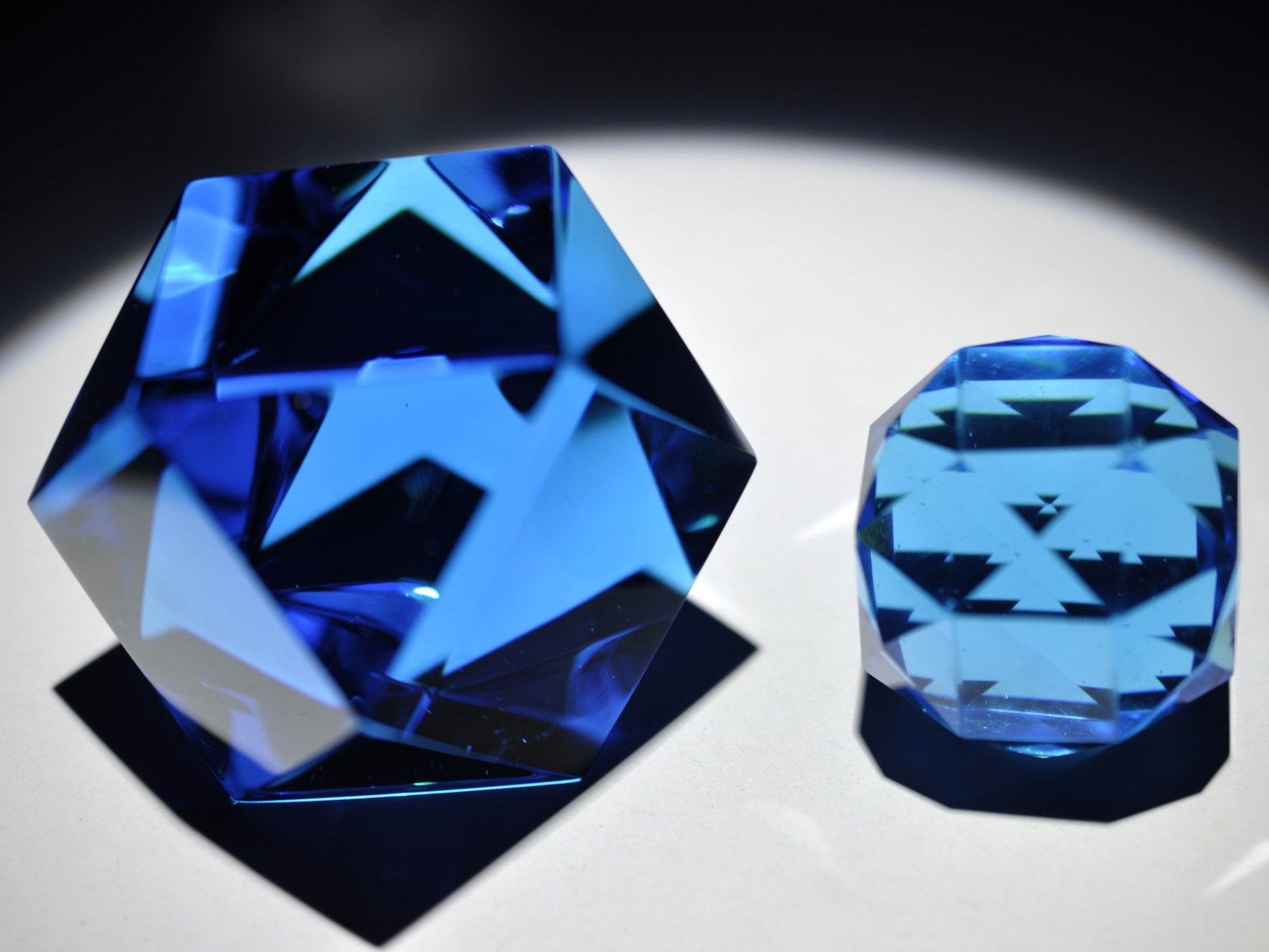 Two Faceted Blue Glass Paperweights: Attributed Brand: Unknown Period: 20th Century Style: Geometric Blocks Base: Clear Largest Diameter: 2.99 in. Combined Weight: 1.22 lb Condition: Small chip on smaller piece, base wear Additional Info