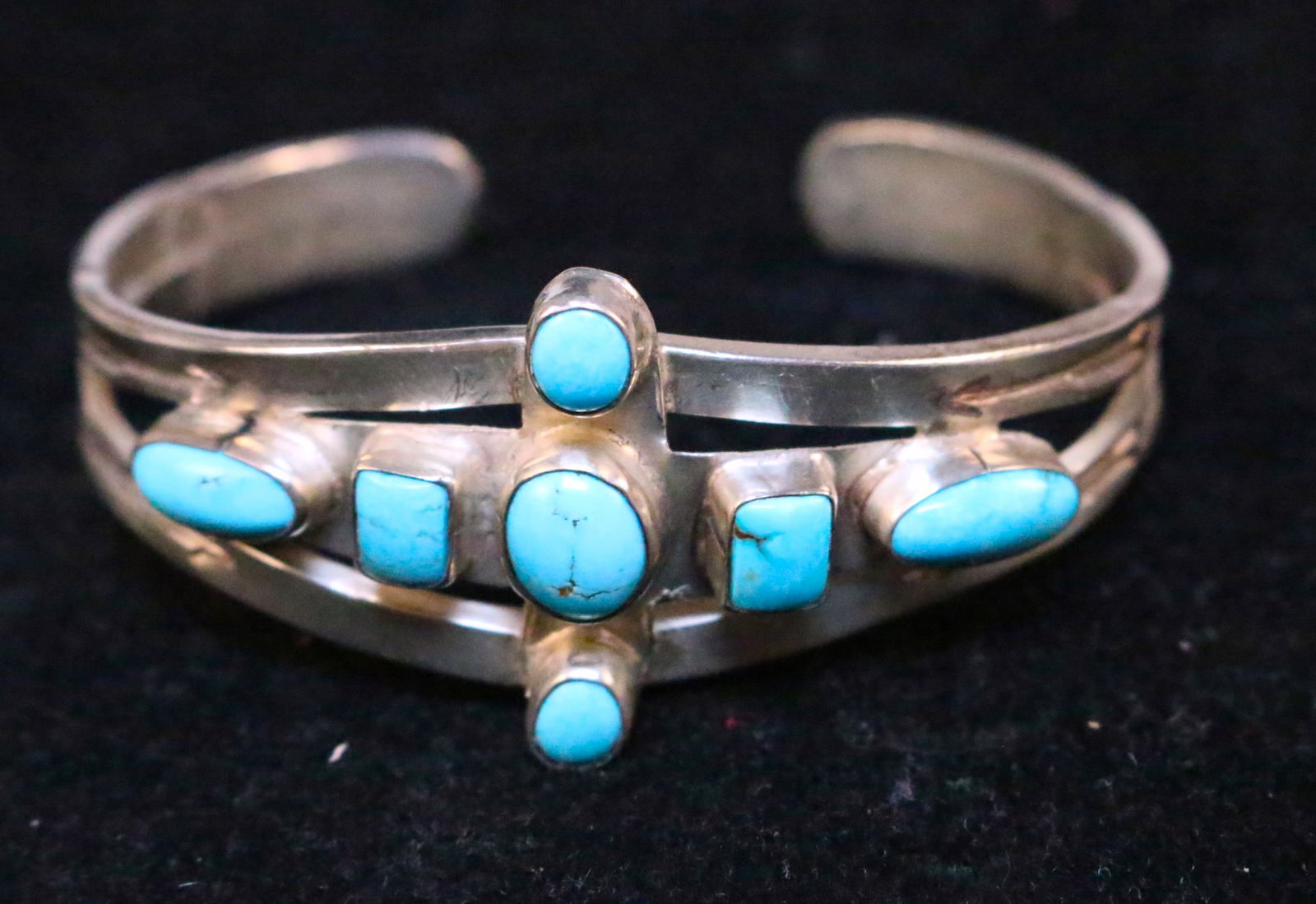 Sterling Silver Native American Southwest Turquoise Cuff Bracelet: Etched Native American design, cross style setting with various shaped turquoise stones ranging in sizes 6mm to 11mm. Weighs 29.3. Inside diameter 6" plus a 1" opening. Cuff thickness is 3/8" at the e